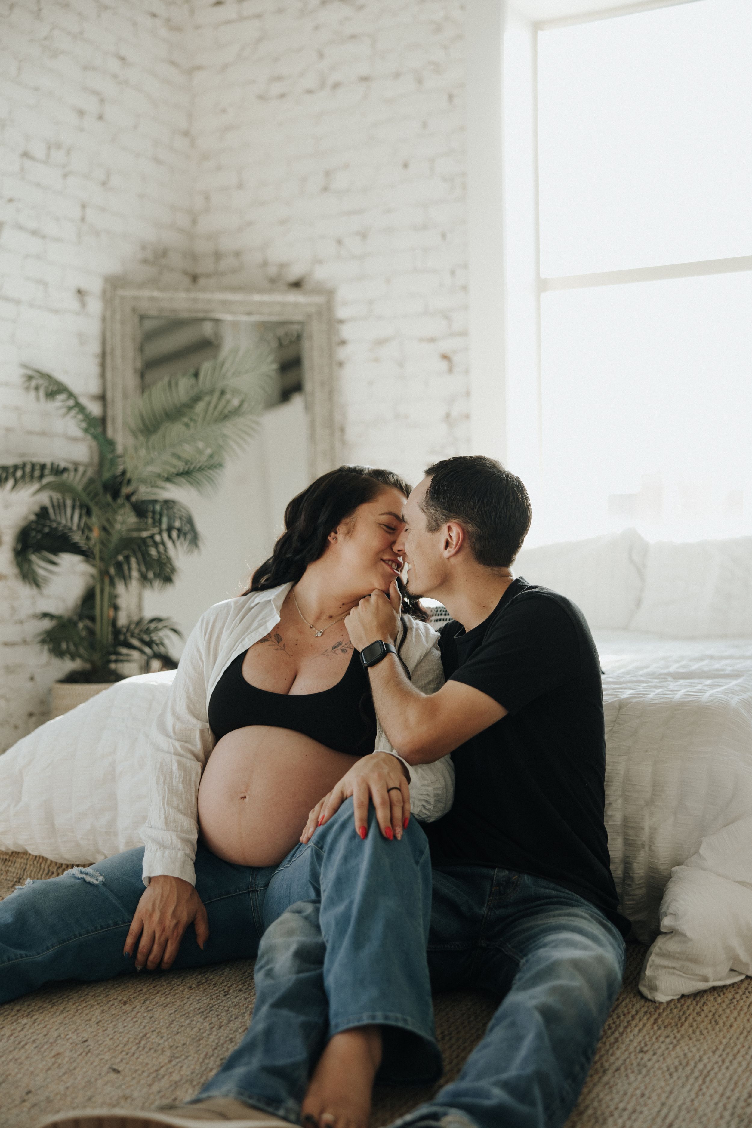 A couple shares intimate moments together on the floor of a bright minimalist room with white brick walls and potted plants.
