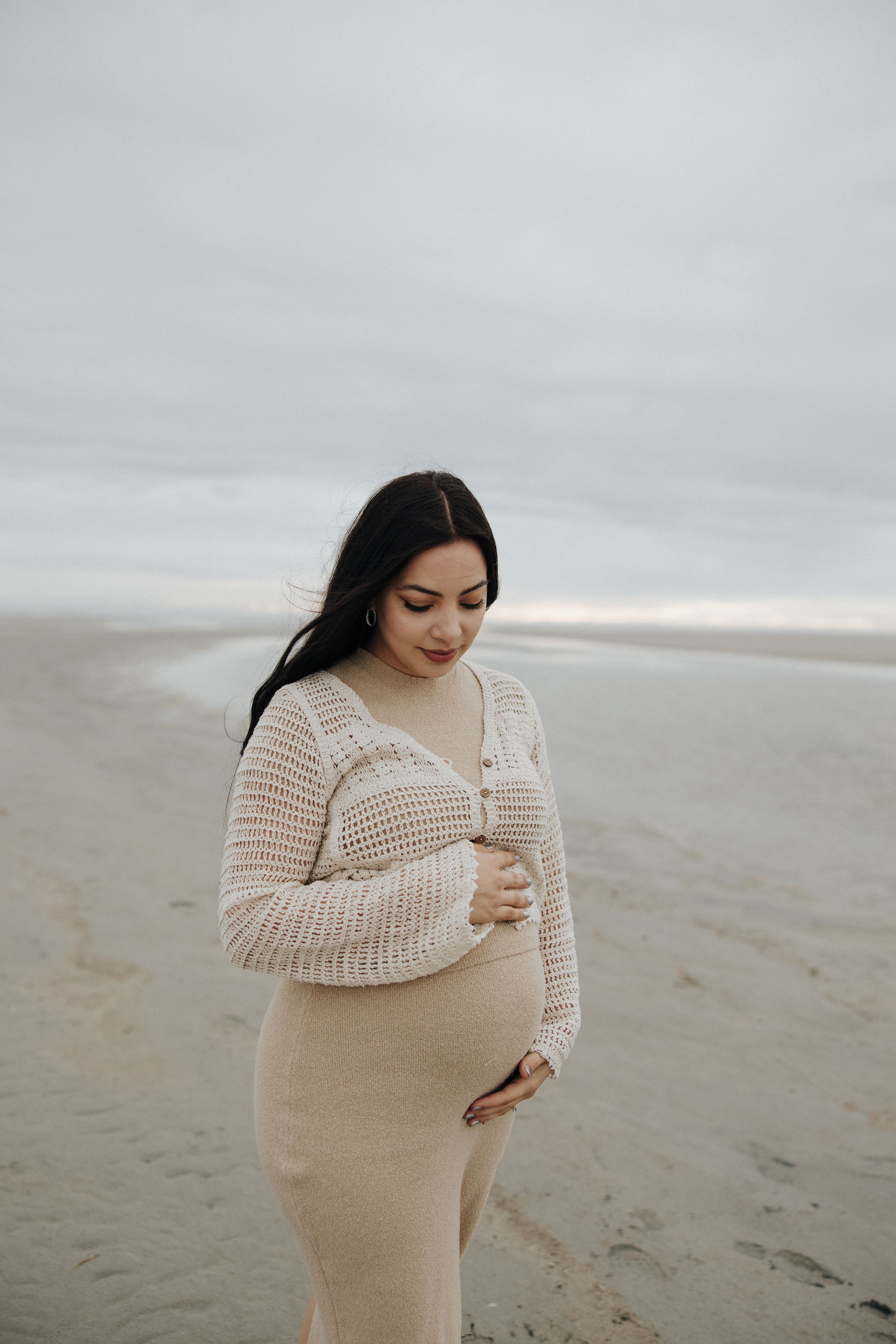 A person wearing a cream knit sweater stands thoughtfully on a misty beach.