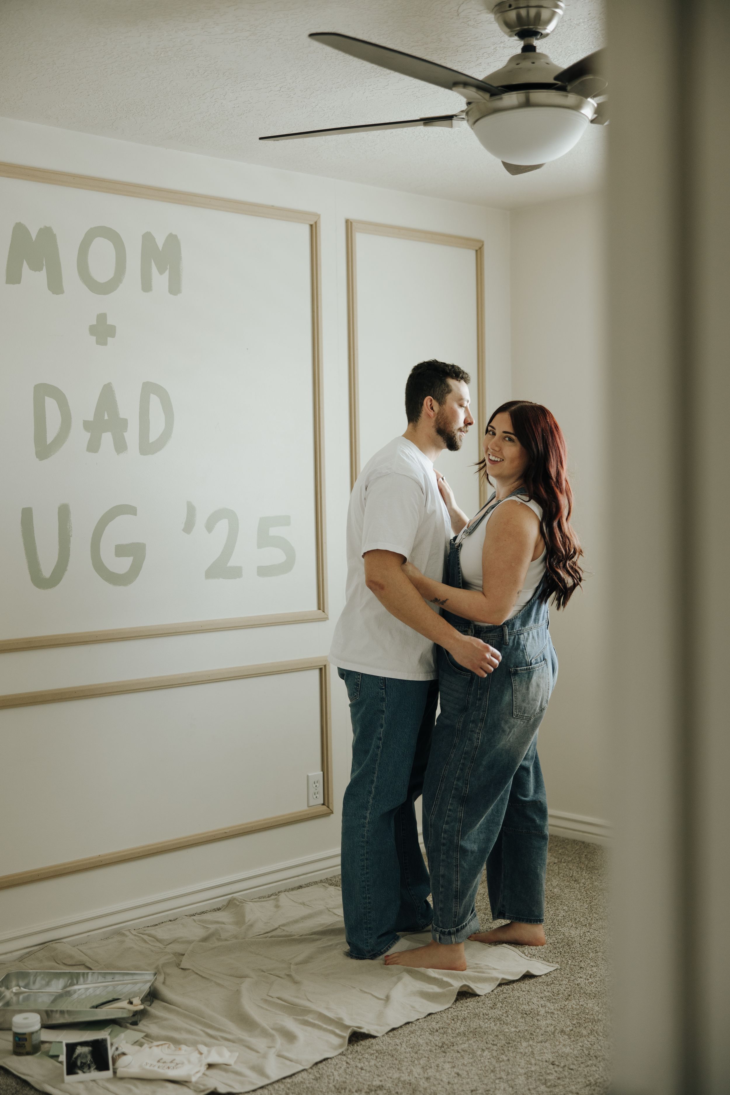 A couple embraces on the floor during an intimate indoor photoshoot with text on the wall.