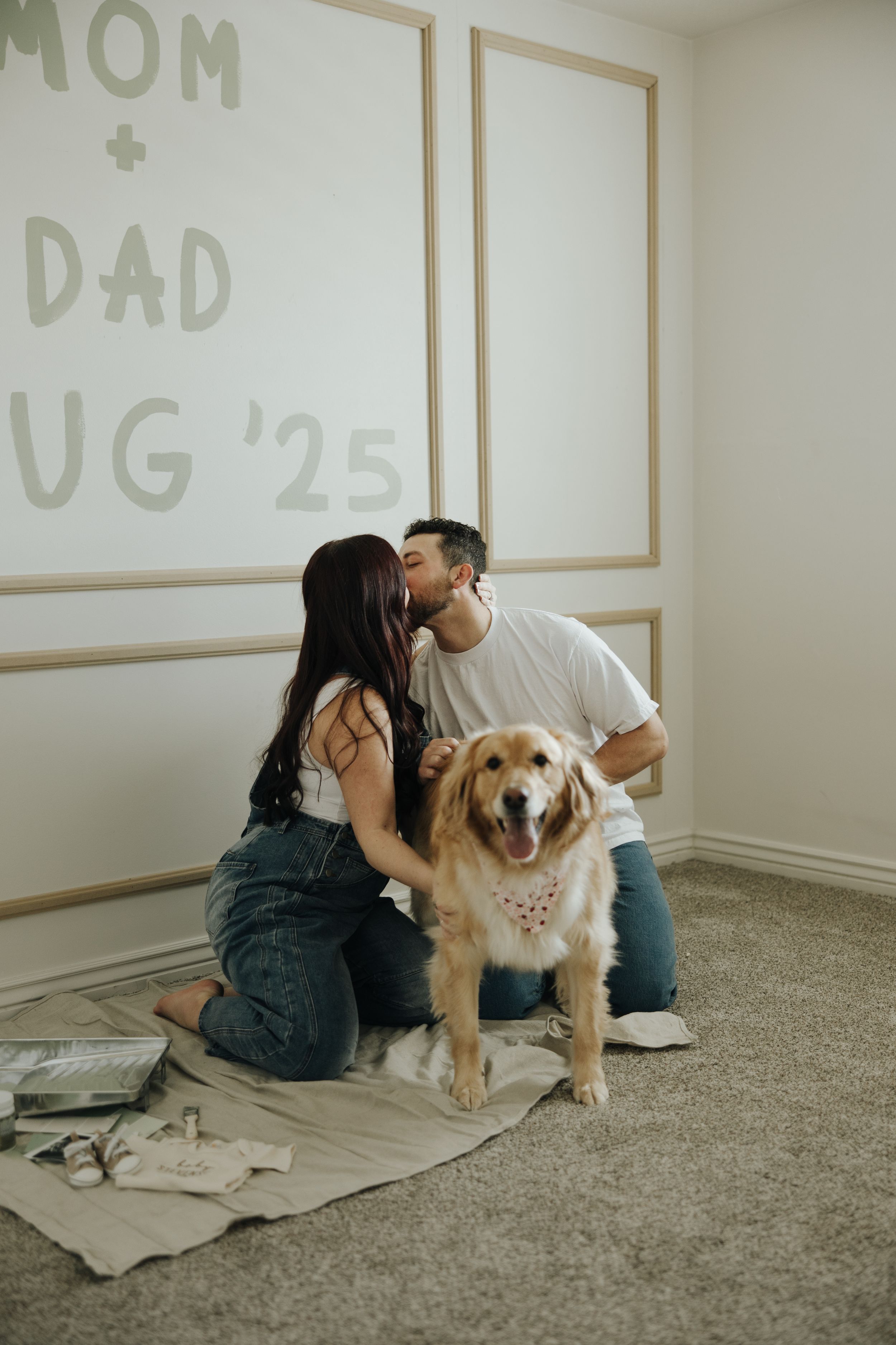 A couple and their golden retriever dog sit on the floor during a pregnancy announcement photoshoot.
