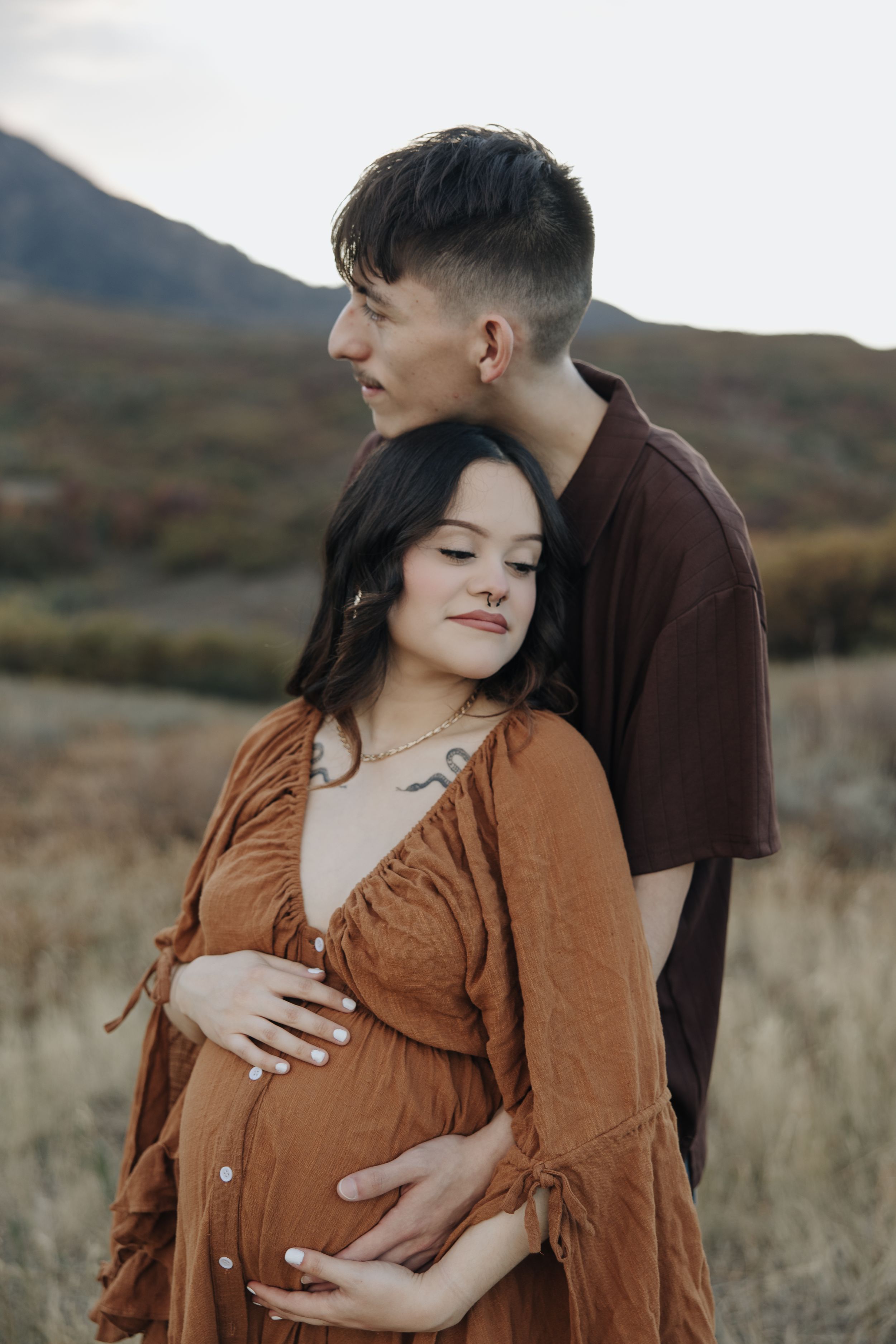 A tender maternity photoshoot moment captured against a mountainous autumn landscape.