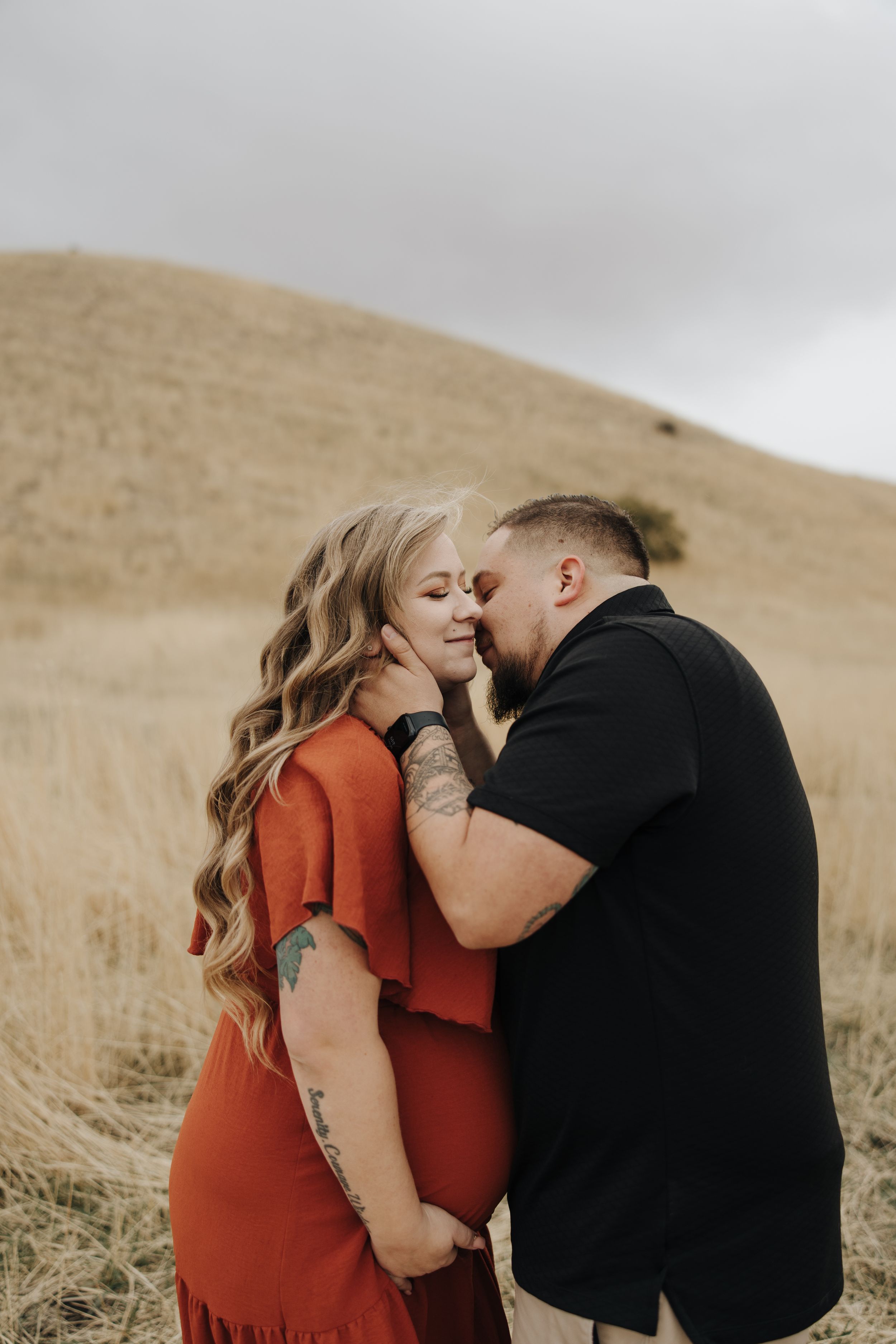 A romantic couple embraces in front of a golden hillside during an intimate outdoor photo session.