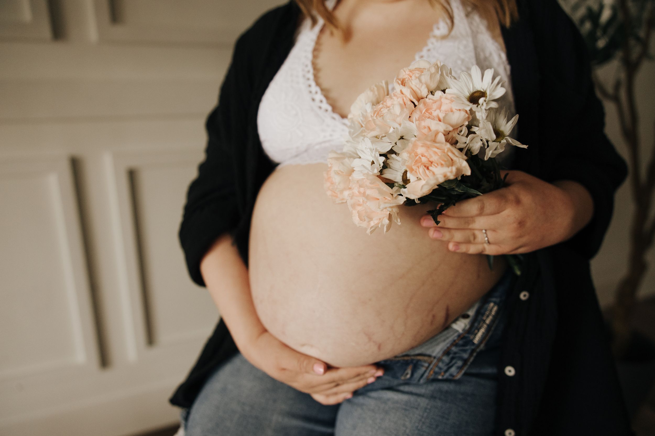 Indoor maternity photo showing pregnant belly with delicate peach and white flowers.