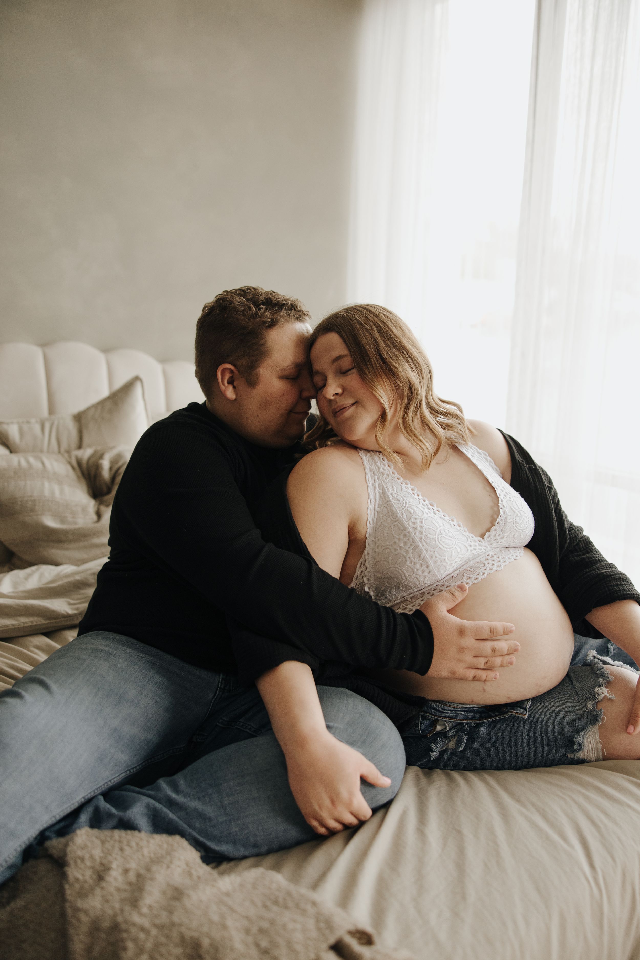 Intimate indoor maternity portrait of couple sharing tender moment on white couch.