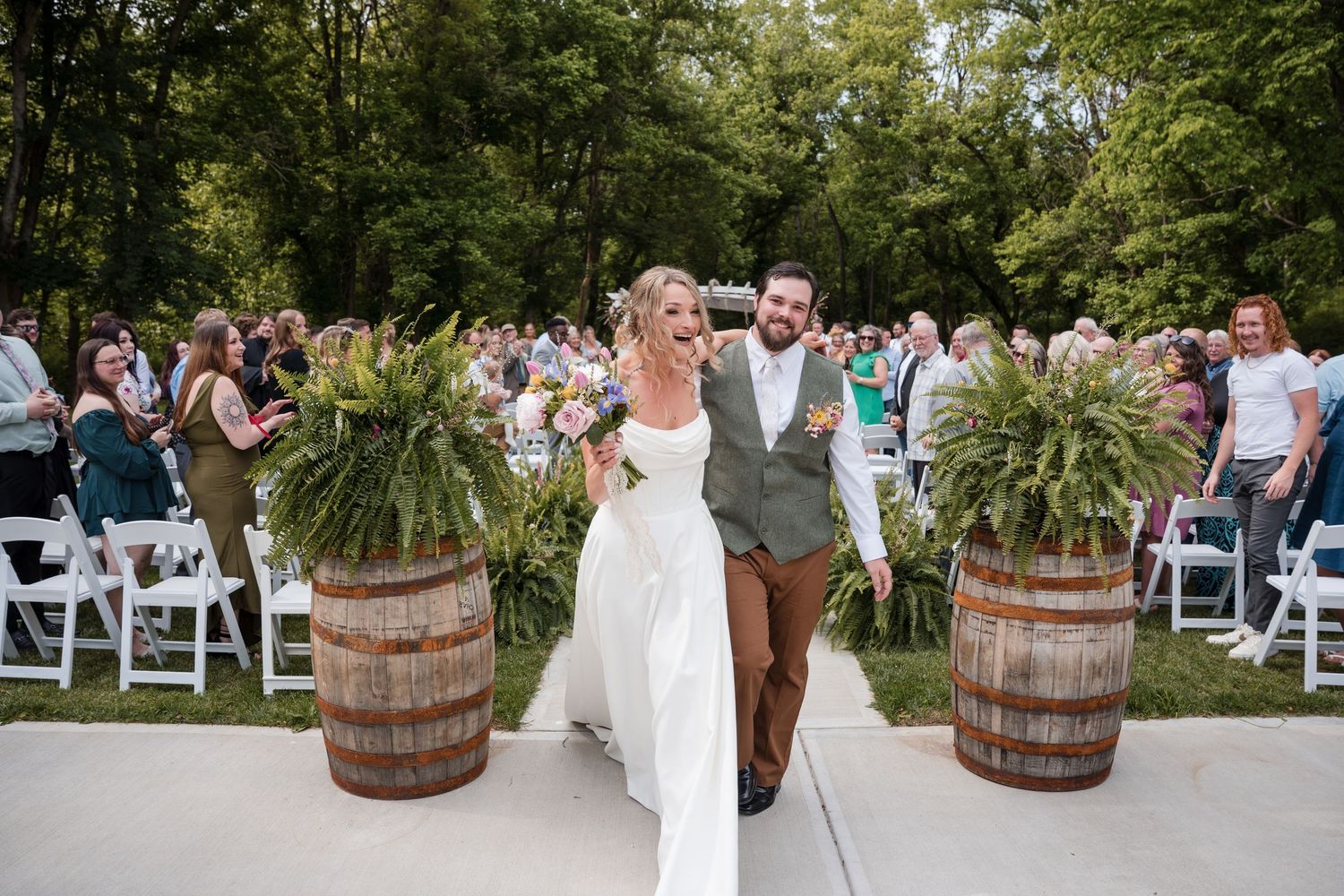 Joyful wedding couple laughing together on autumn path with rustic bouquet.