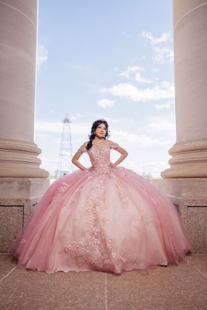 Stunning pink quinceañera ball gown with intricate lace details framed between classical stone columns.