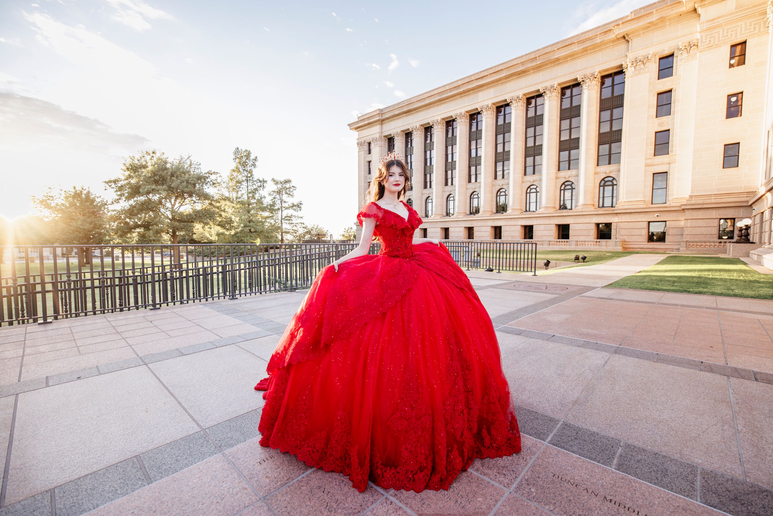 A dramatic red ball gown photographed against modern architecture at sunset.