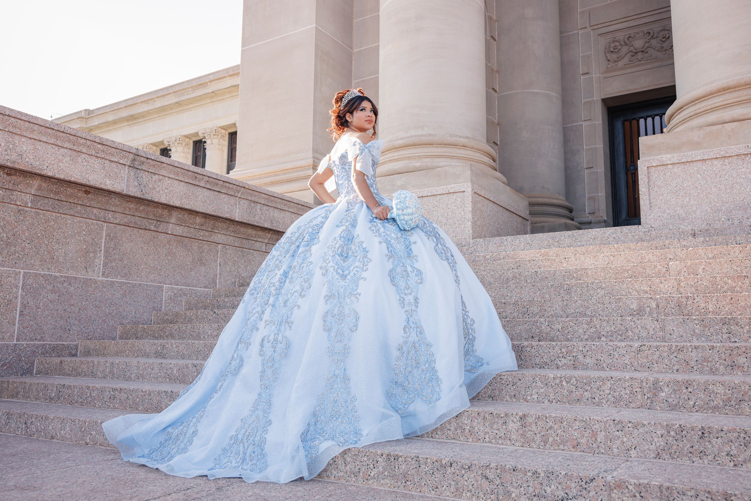 Powder blue ball gown with intricate embroidery photographed on stone steps.