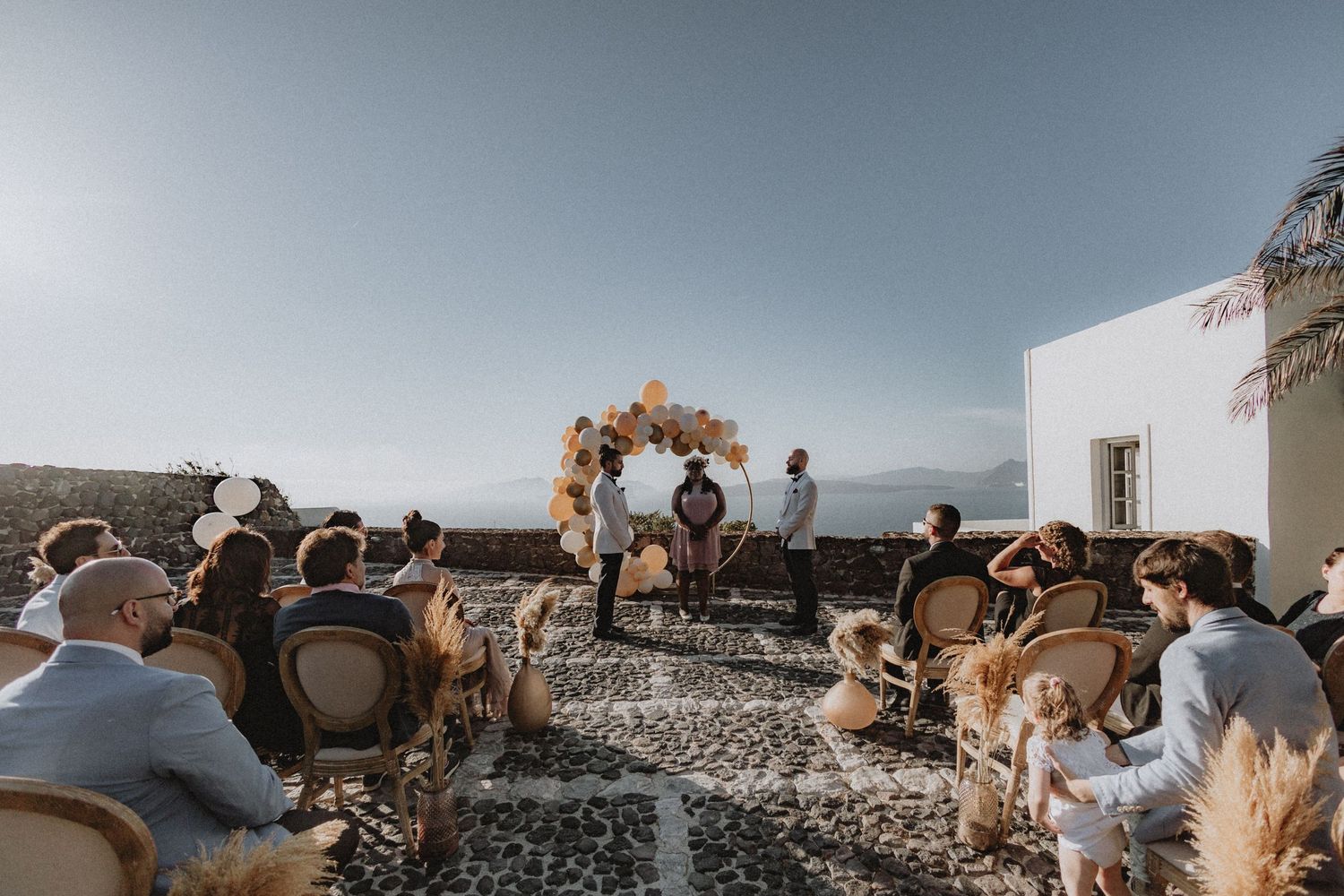 Two grooms getting married with a balloon arch backdrop overlooking Santorini see in Greece.