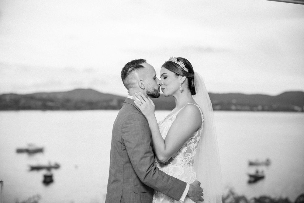 Romantic black and white portrait of newlyweds embracing with boats on the water in background.