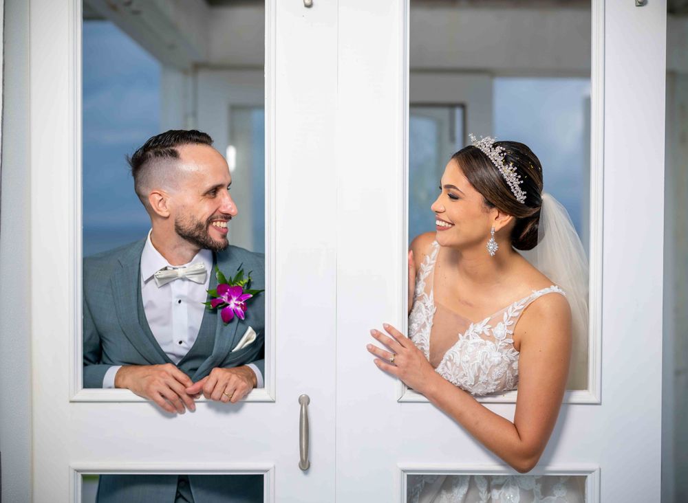 Joyful wedding couple sharing a laugh through white window frames.