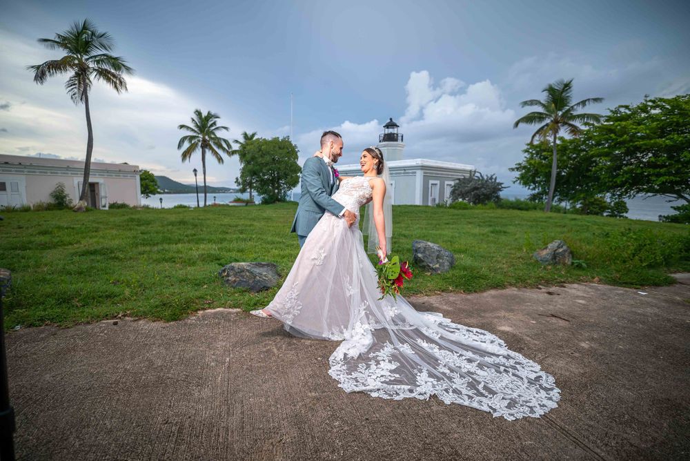 Newlyweds pose outdoors with long lace wedding dress train and palm trees in tropical setting.