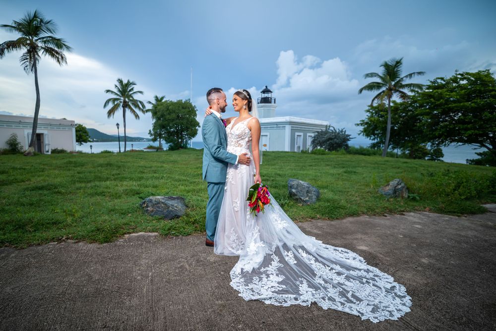 A scenic tropical wedding photo with palm trees and a stunning lace train dress on a coastal path.