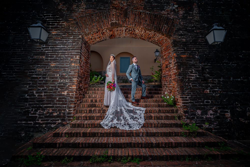 A dramatic wedding portrait under a brick archway with vintage lanterns and stone stairs.