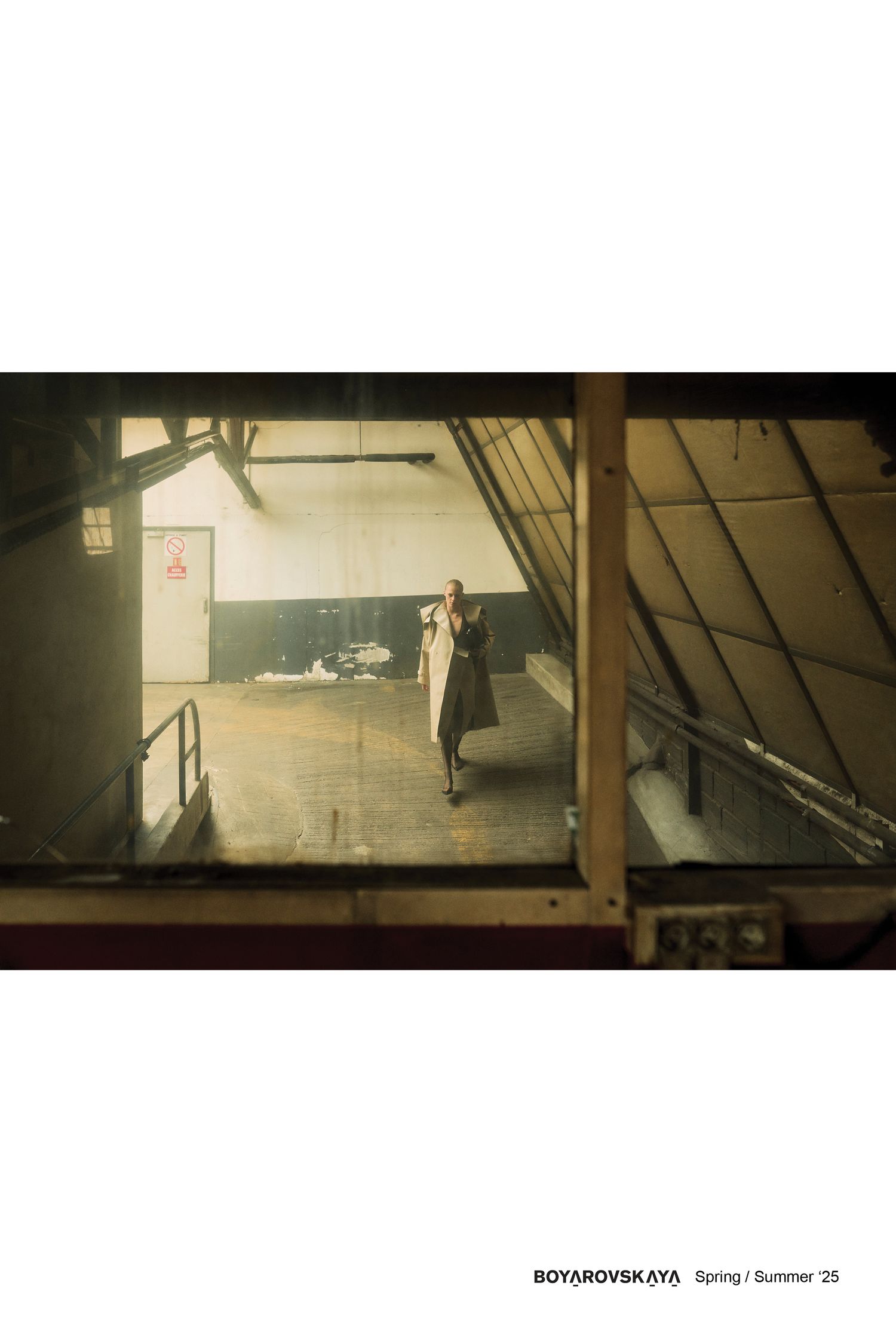 Vue à travers une fenêtre industrielle montrant une figure en robe blanche dans un espace d'entrepôt vide.