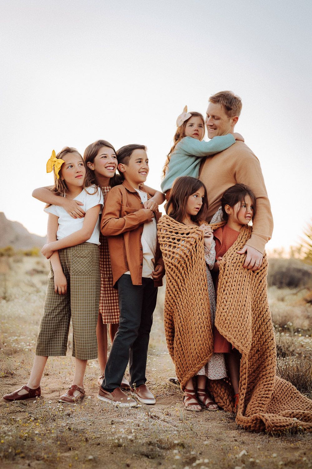 Father joyfully embracing his children in the Joshua Tree desert, surrounded by natural scenery and mountains at sunset.