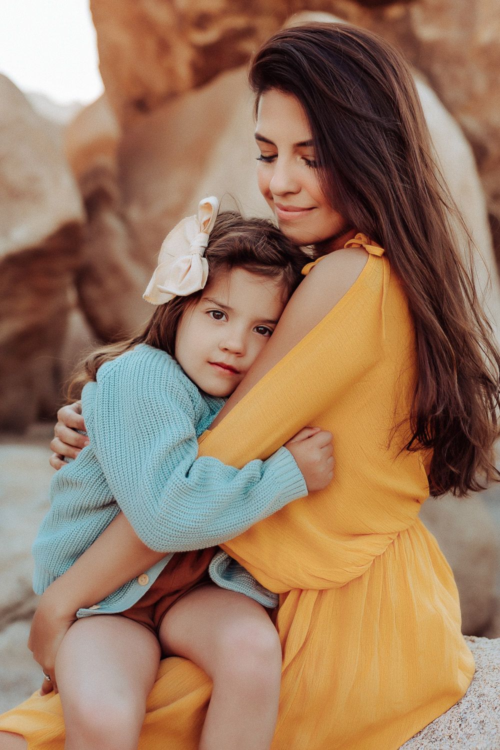“Mother and daughter holding hands in the Joshua Tree desert, sharing a tender moment with a scenic Joshua Tree, CA.