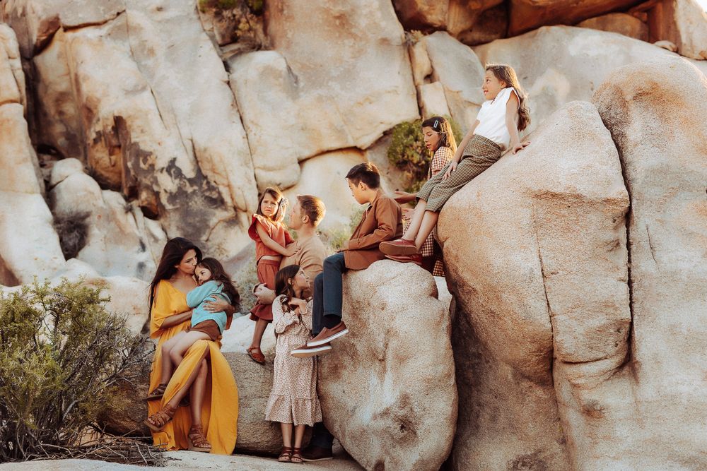 Family of eight embracing in the Joshua Tree desert at sunset, with mountains in the background