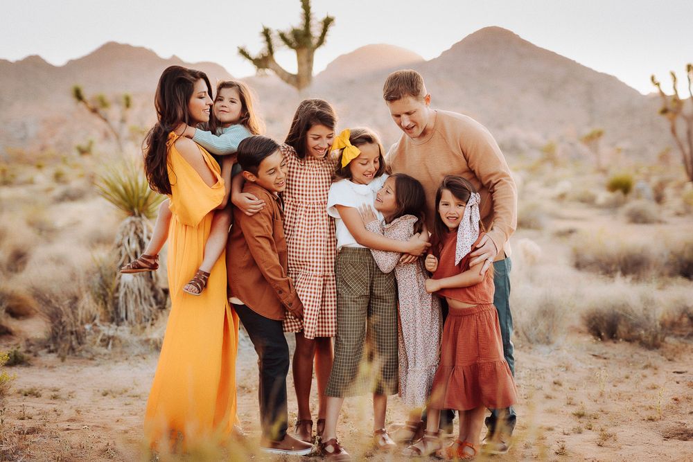 Parents and six children hugging in the Joshua Tree desert, a heartwarming family moment at sunset
