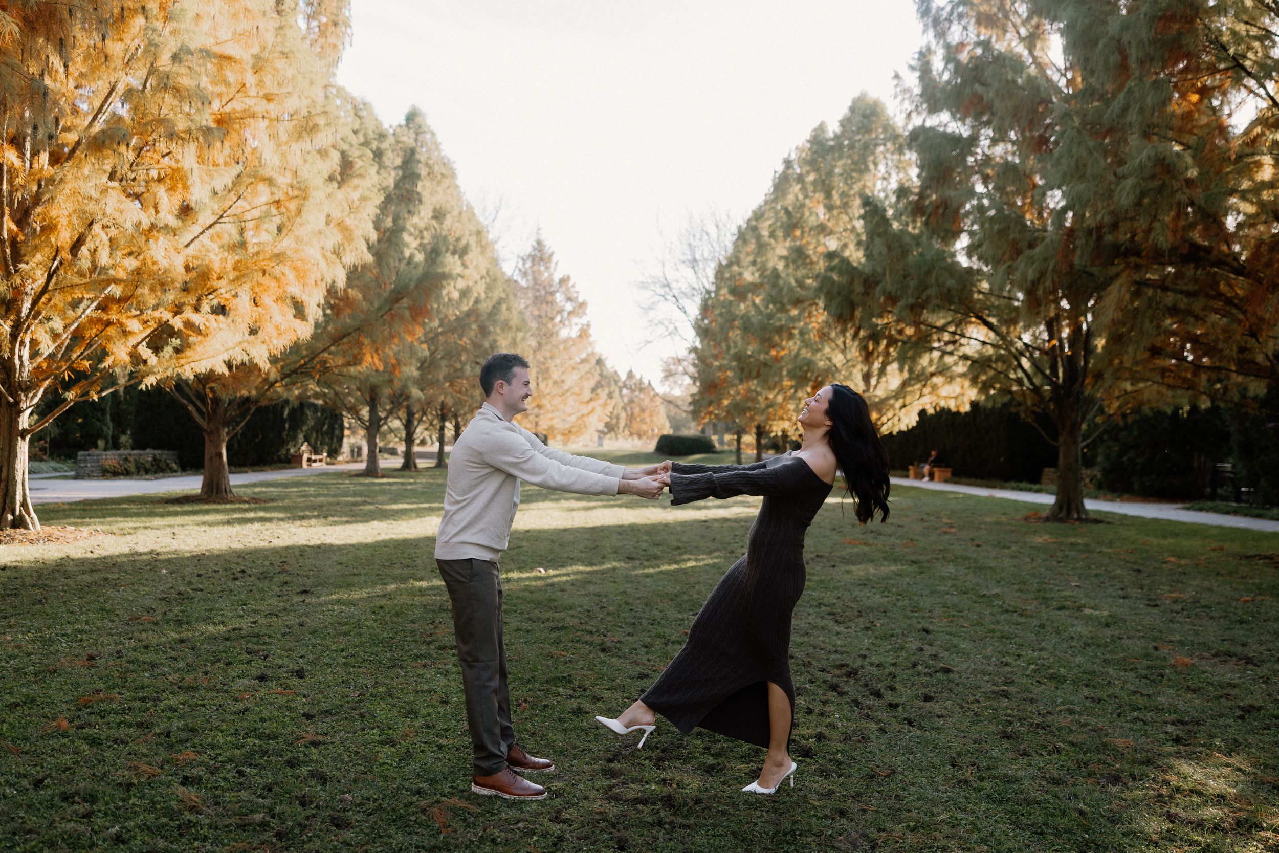 Candid wedding party moment captured in golden sunlight on grassy lawn.