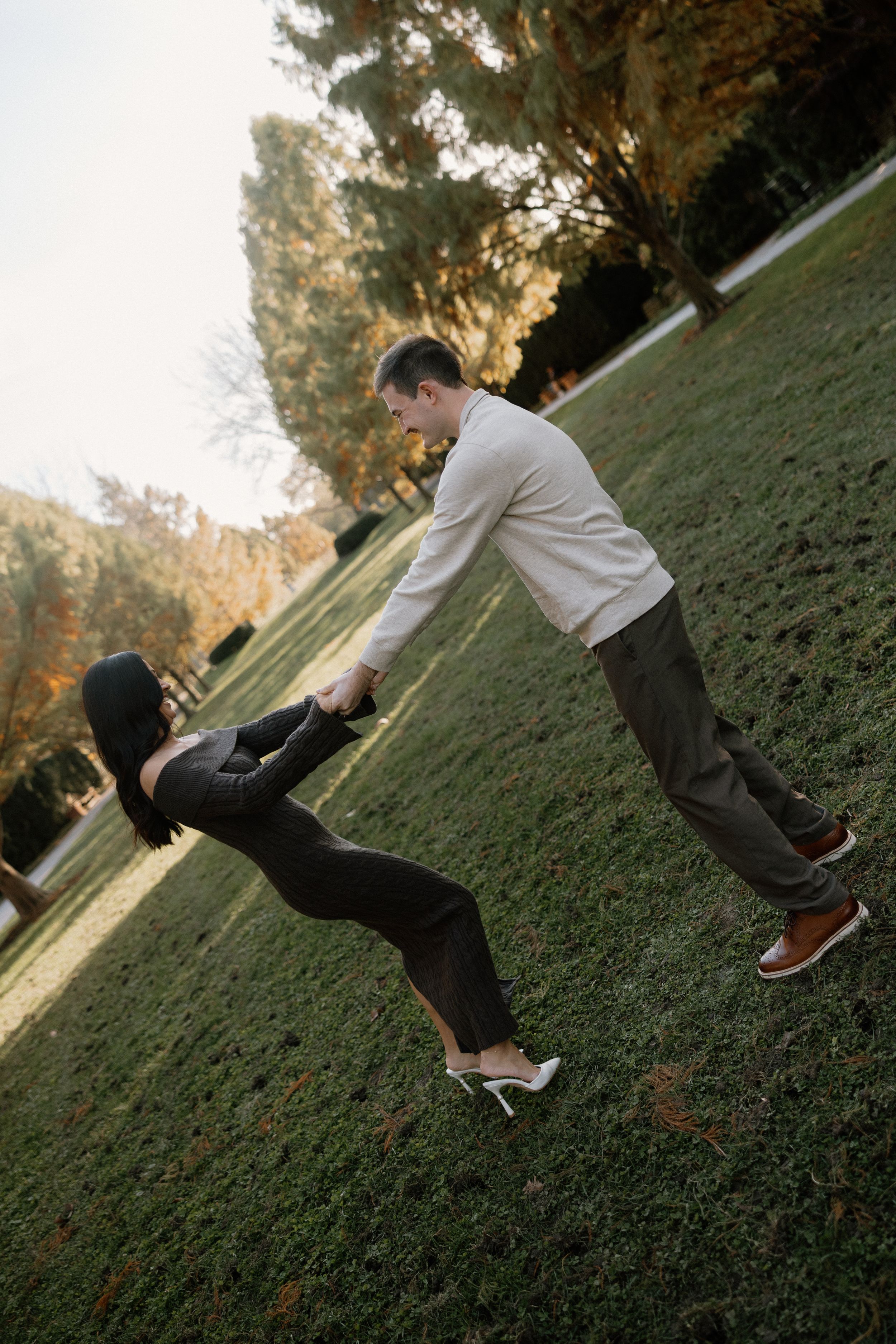 A couple plays together on a grassy hillside during a golden sunset.