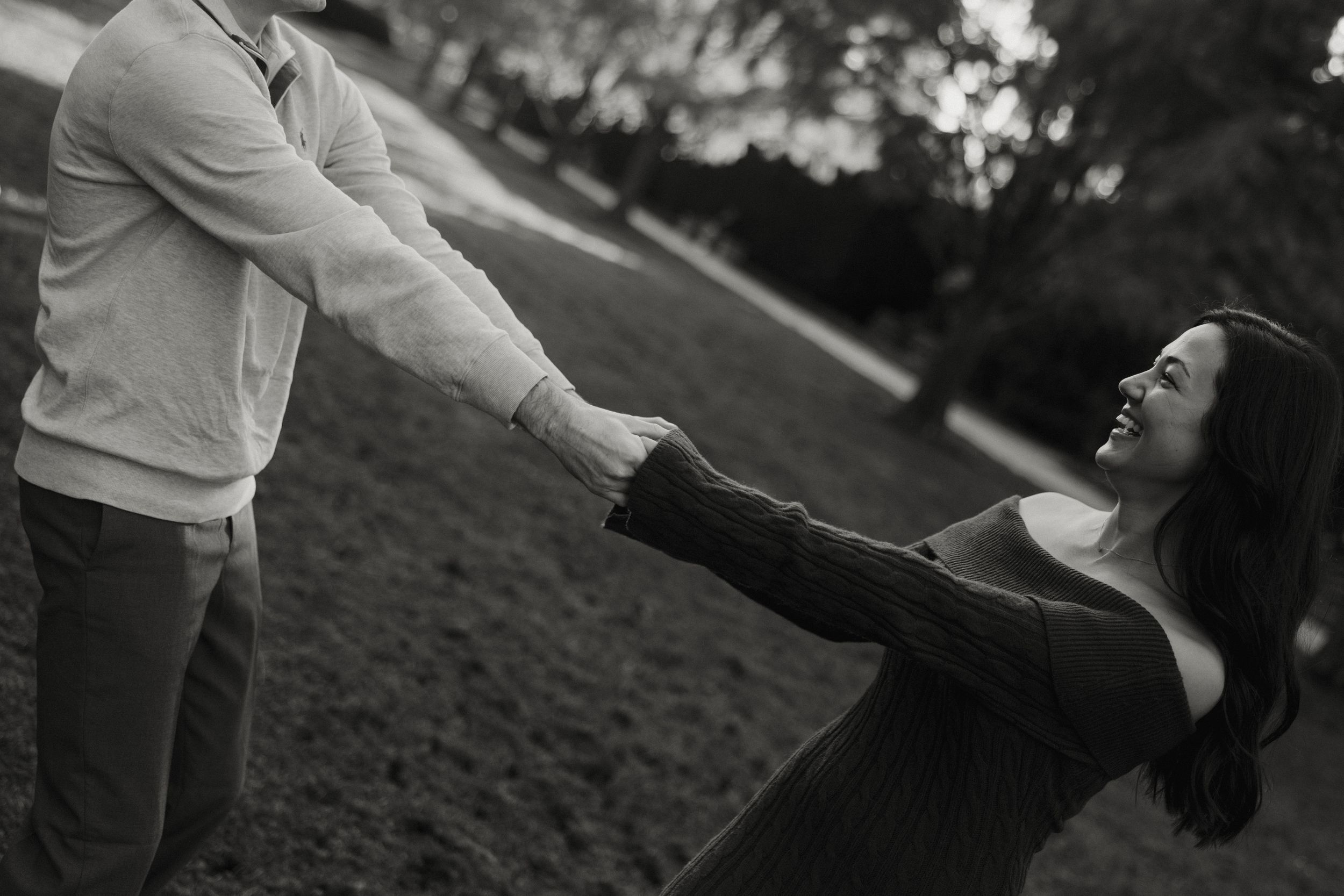 A couple shares a playful moment together on a grassy hill in black and white.