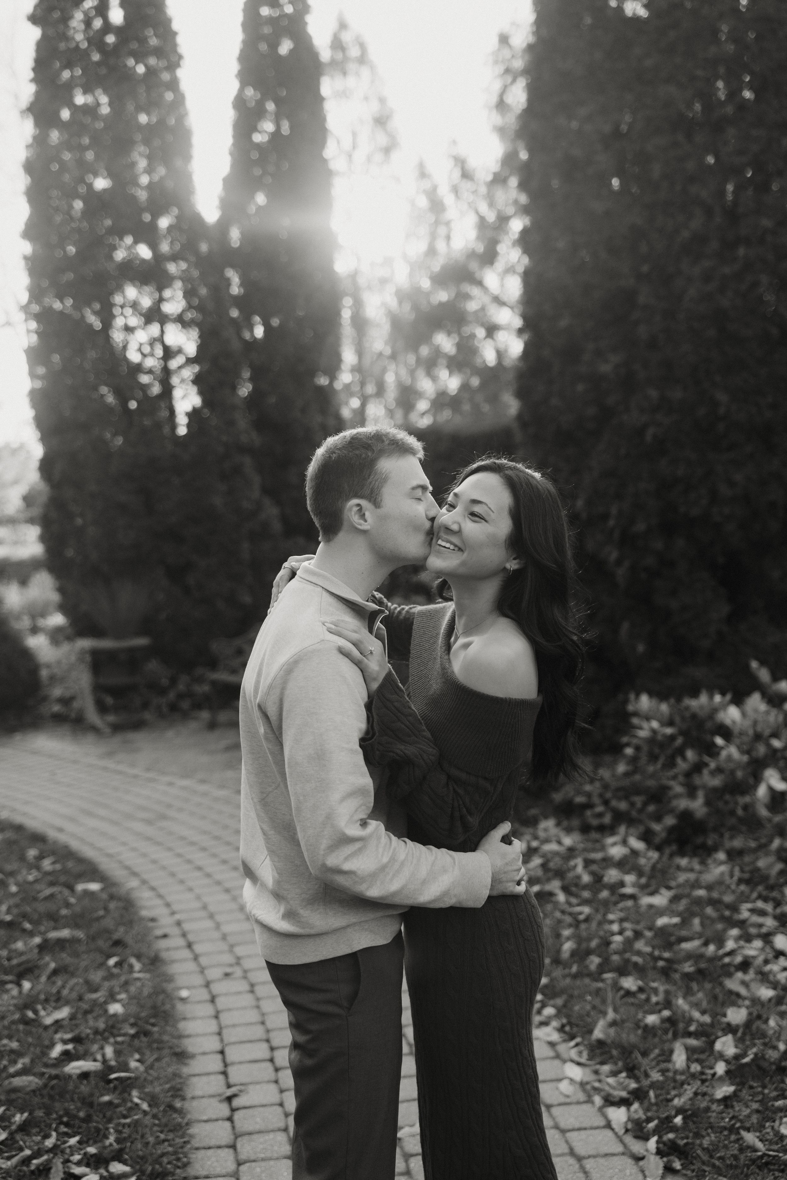 A romantic moment captured between a couple on a stone pathway with evergreen trees in the background.