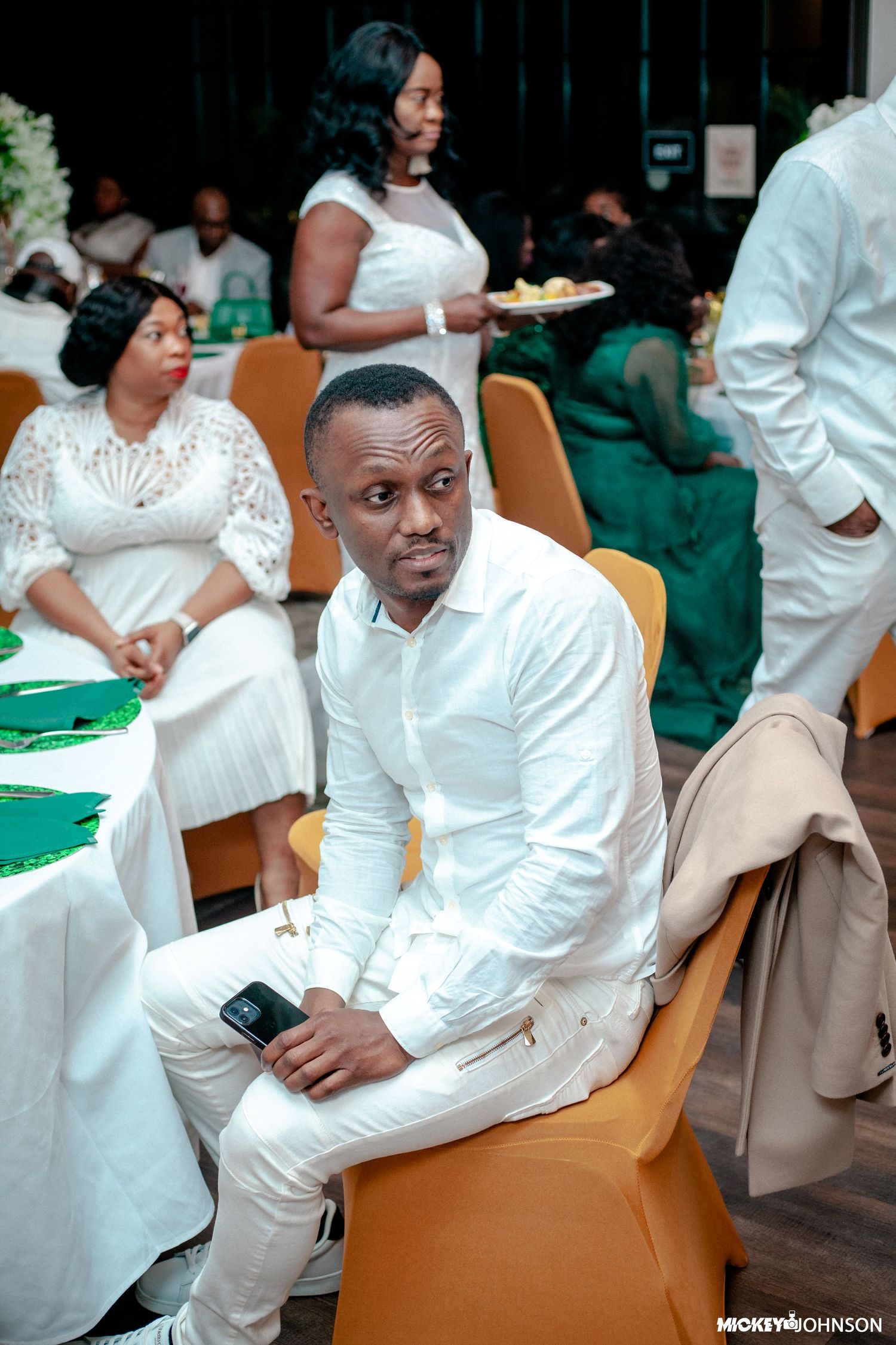 Guests in white attire seated at tables with green tablecloths.