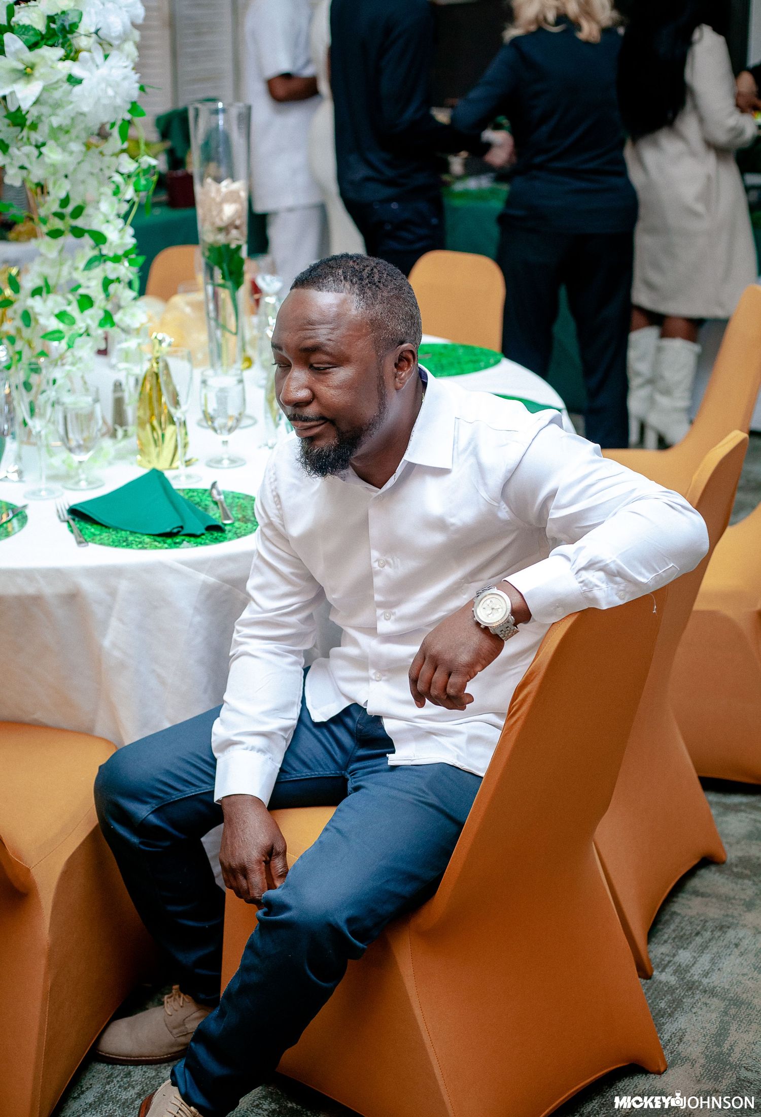 Person in white shirt seated in orange chair at event.