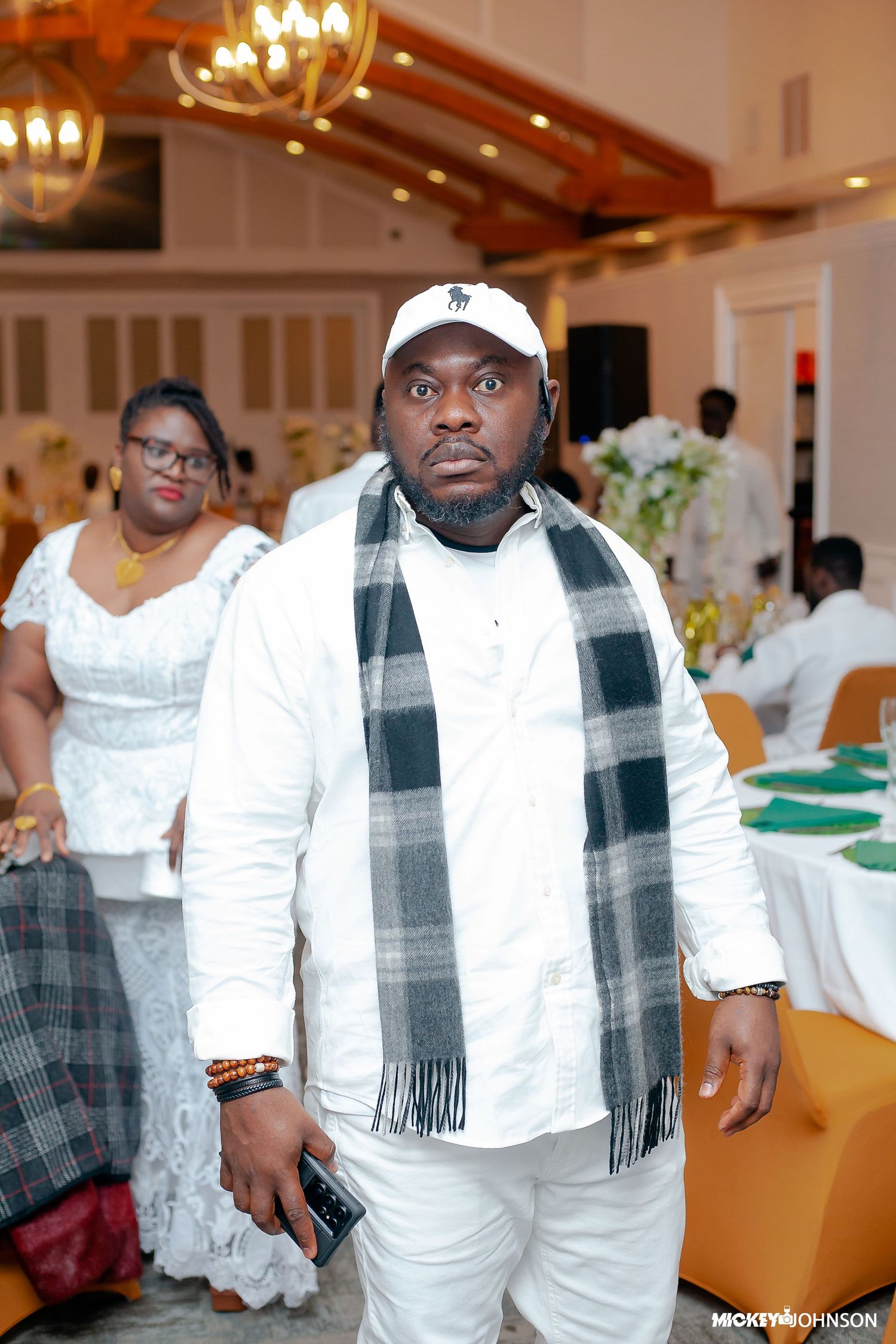 Group in white attire and plaid scarves at formal gathering.