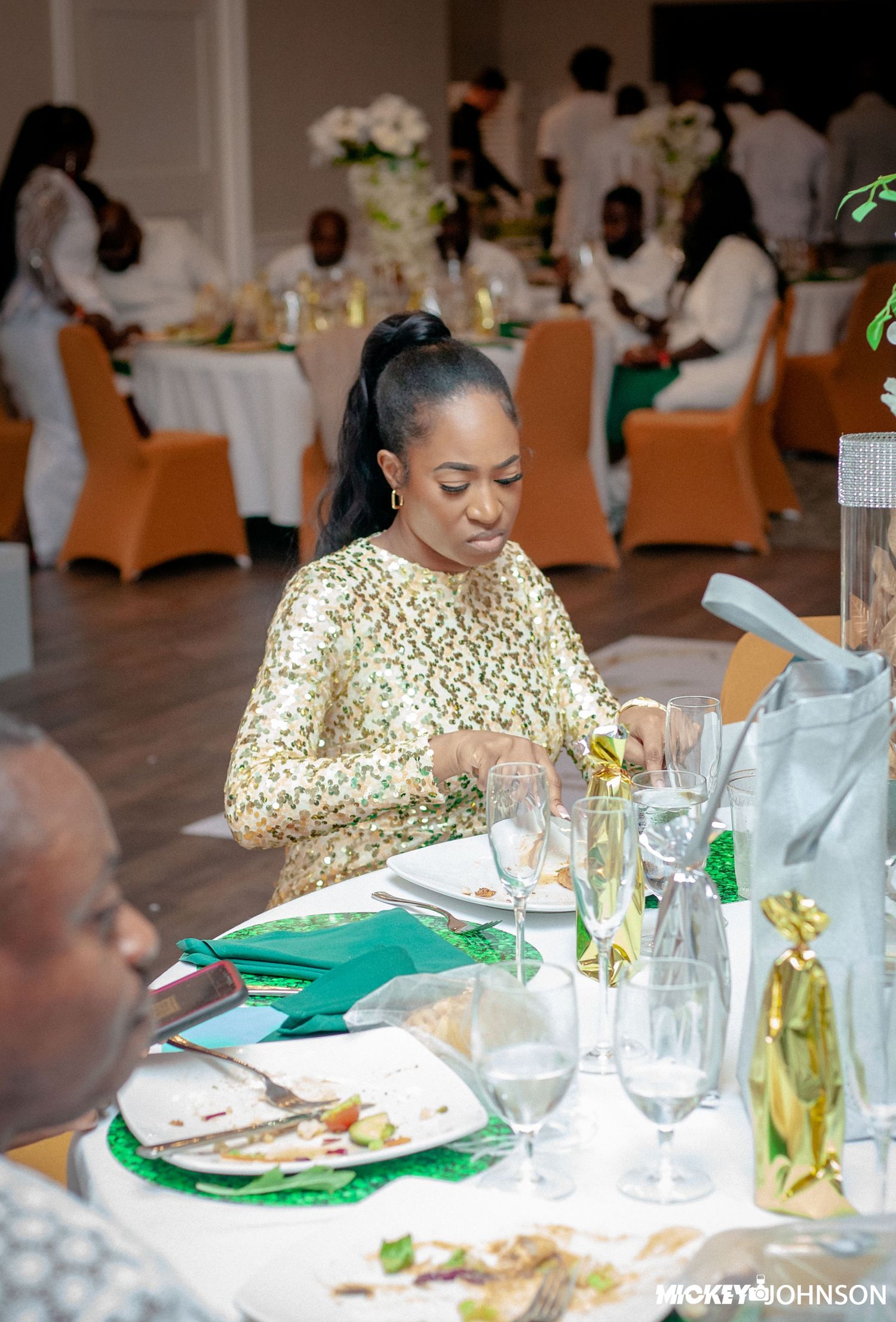 Formal dinner setting with gold and green decor elements on round tables.