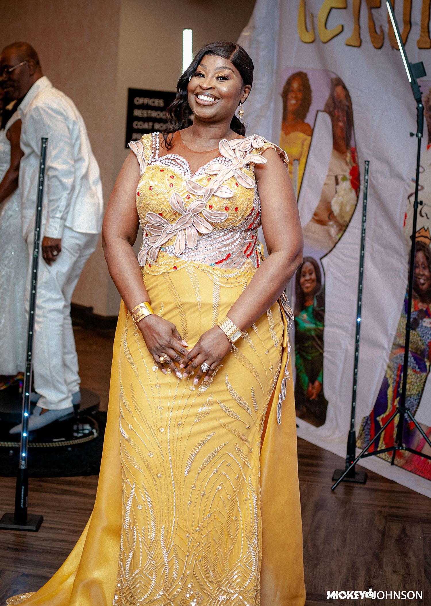 Woman in a flowing yellow formal gown with decorative details posing at an event.