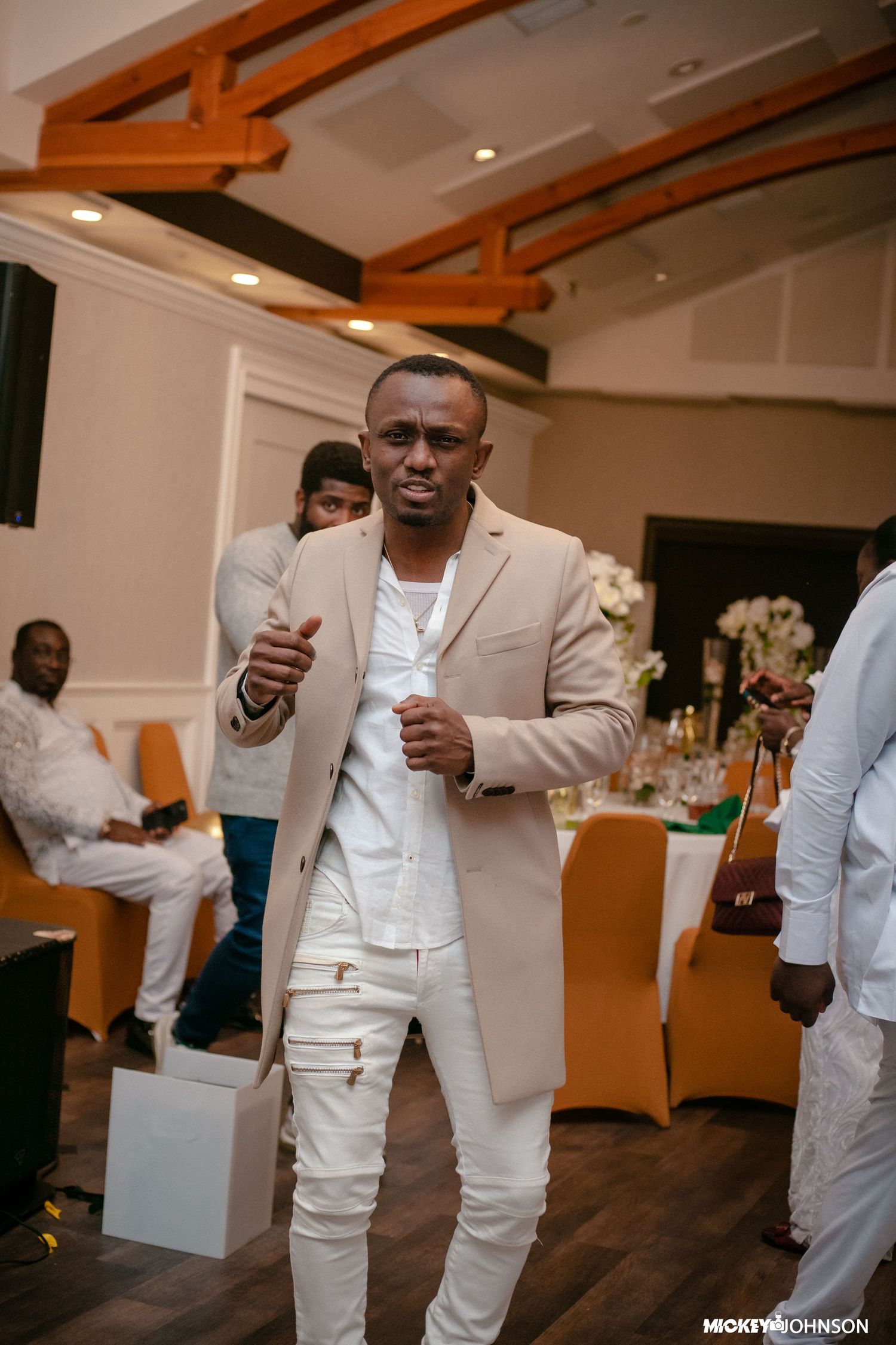 People in all-white formal attire standing and gesturing at an indoor event.