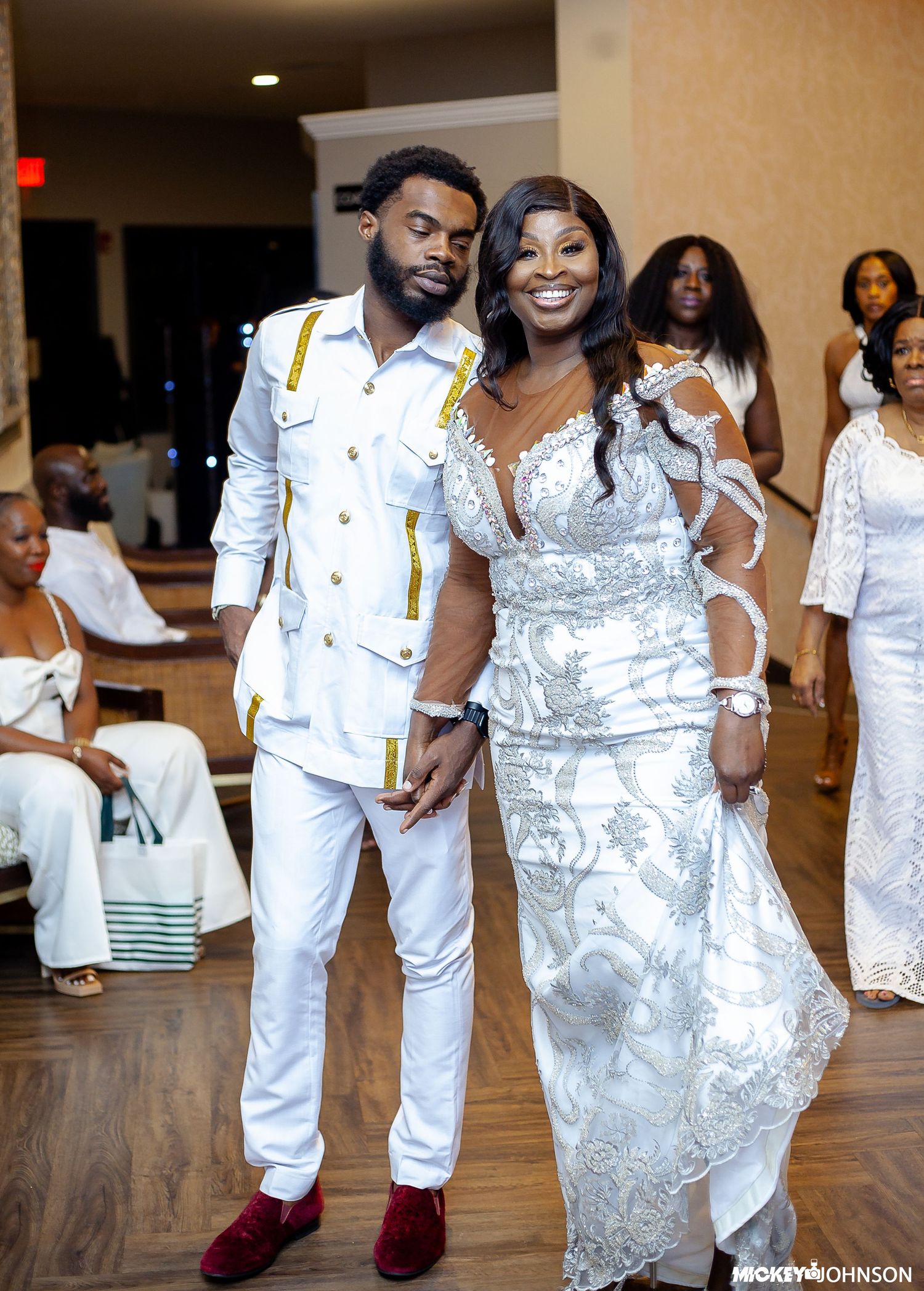 A couple in coordinated white outfits pose together at a formal event.