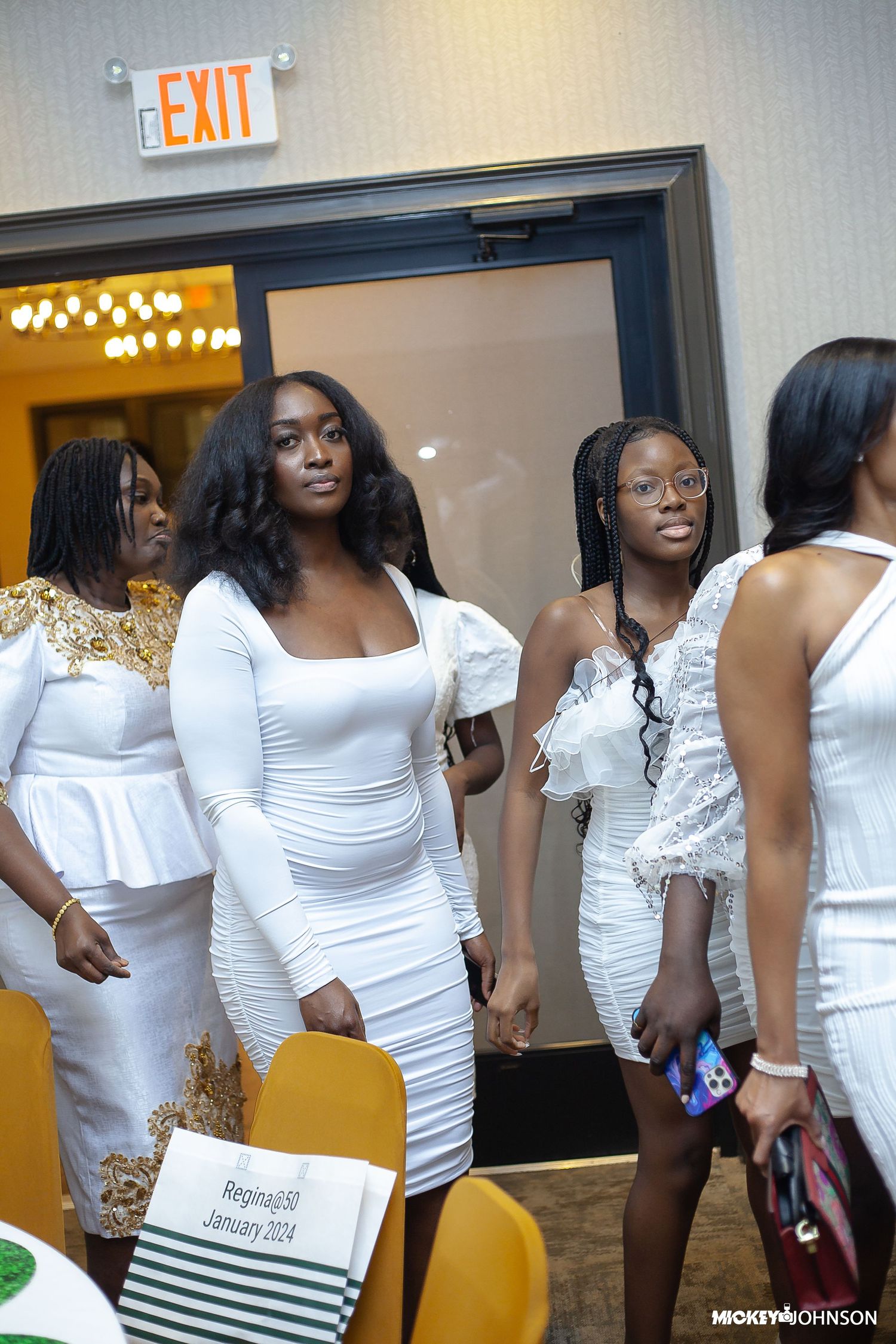 Guests in white dresses and formal attire gathered near an exit sign at an event.