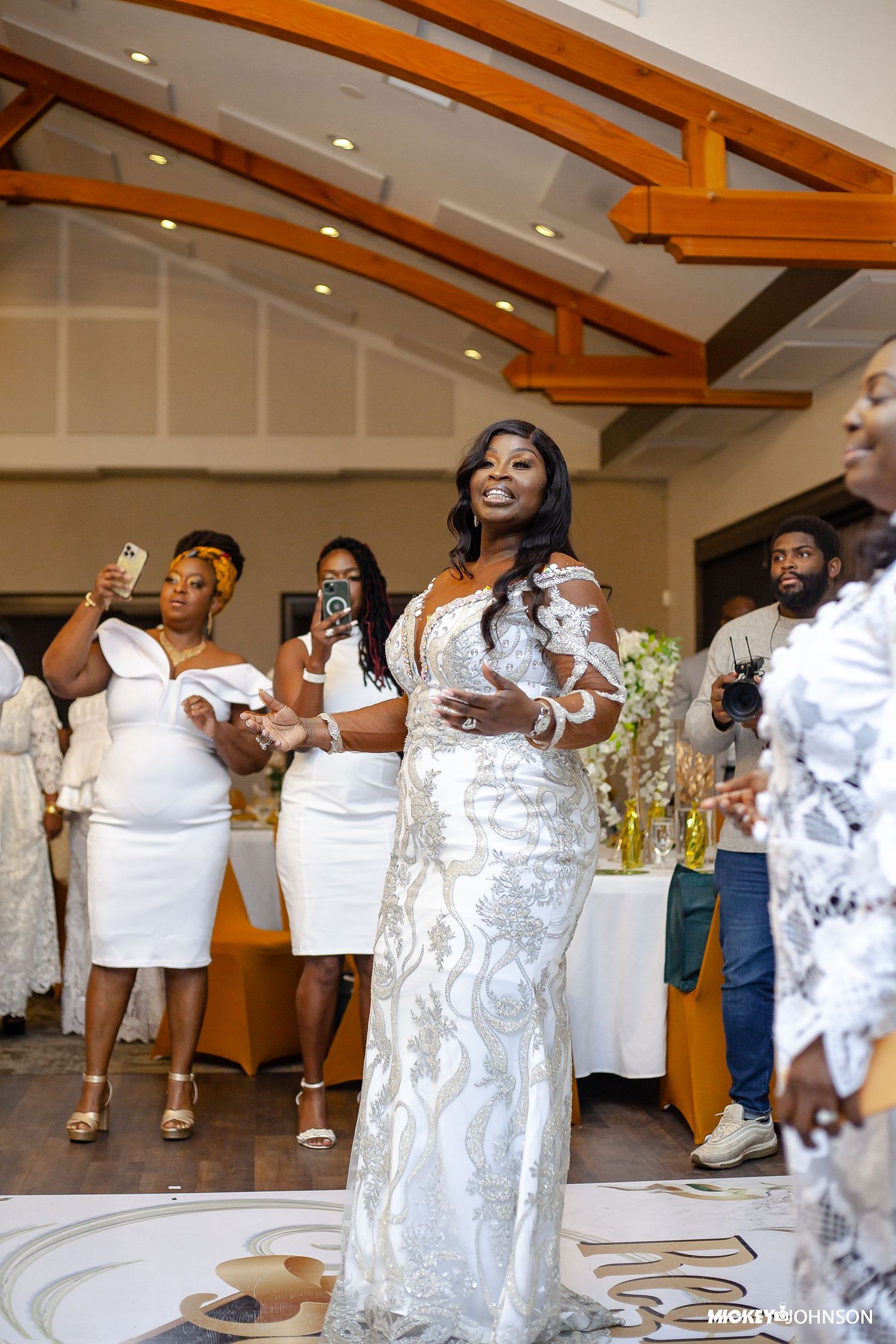 Celebration scene with people in white attire dancing in a room with wooden beams.