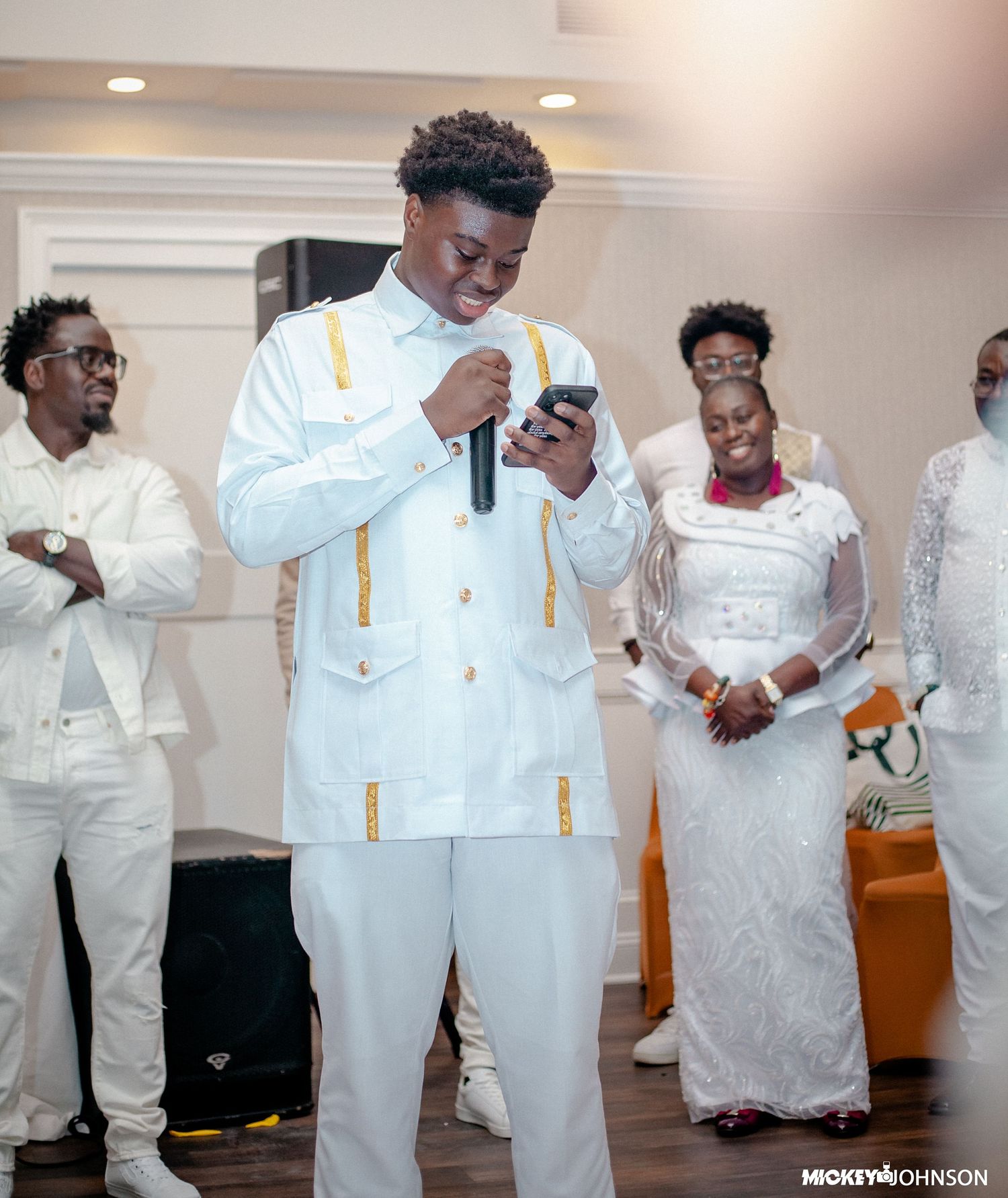 Group in all-white formal wear and suspenders socializing at an indoor venue.