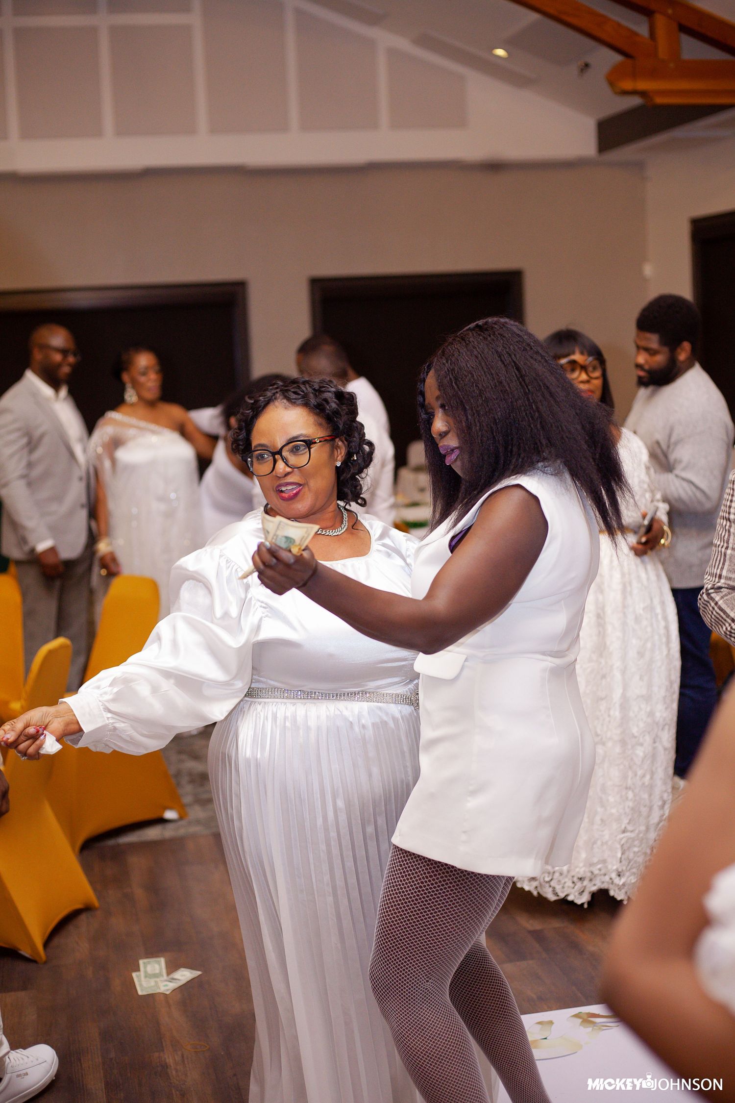 Two guests dance together at an all-white party celebration on a wooden dance floor.
