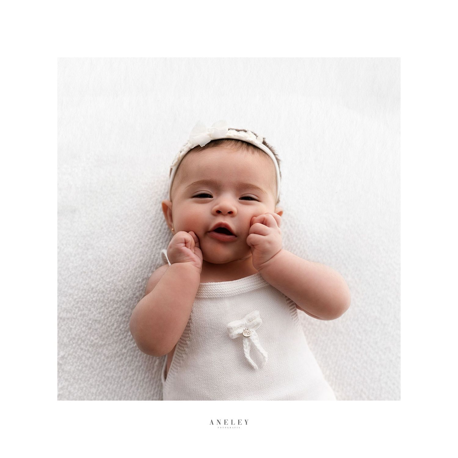 Happy infant wearing white romper and headband smiles during professional photo session.