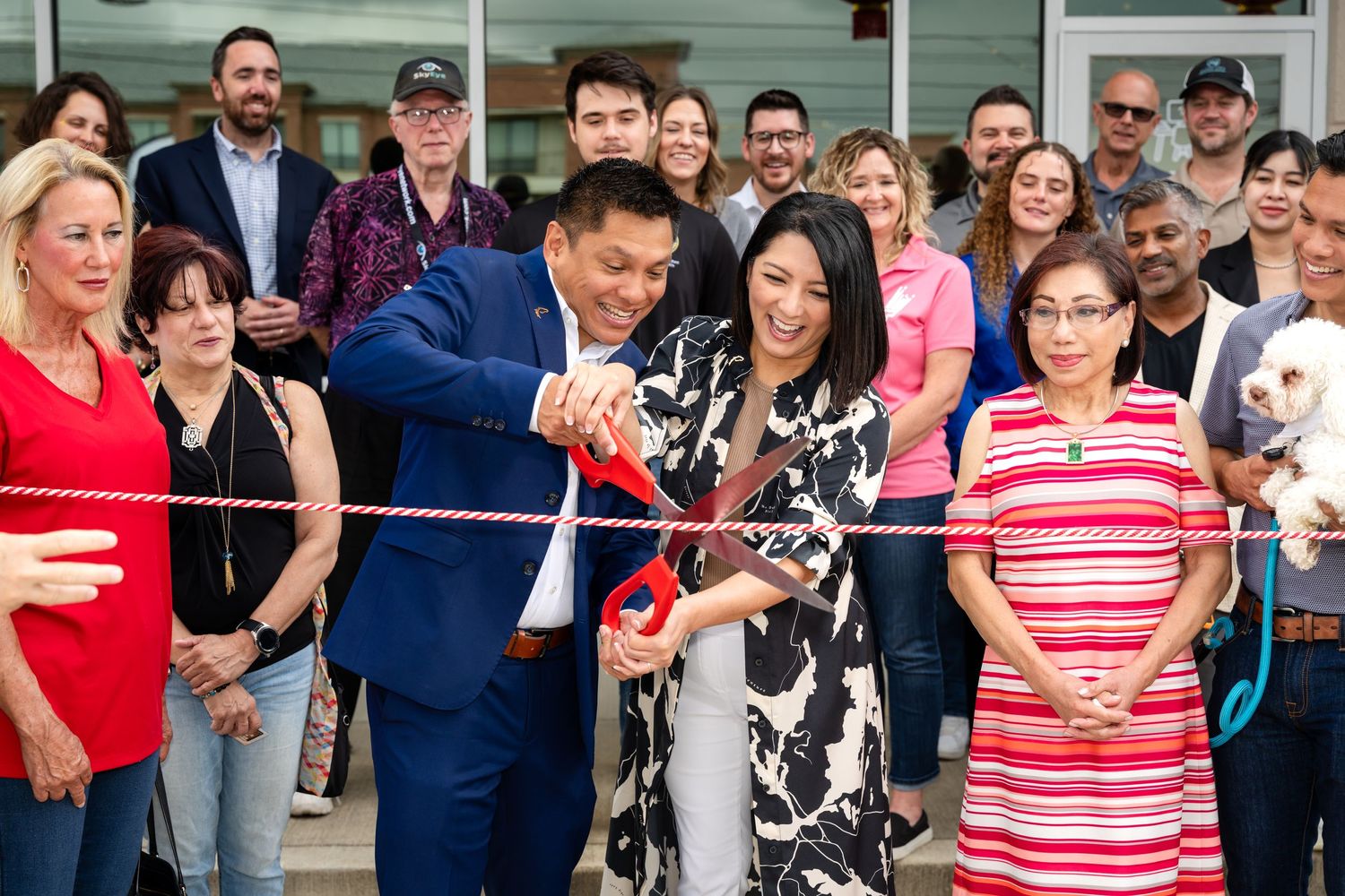 People gather for a grand opening ceremony as two individuals cut a ceremonial ribbon.