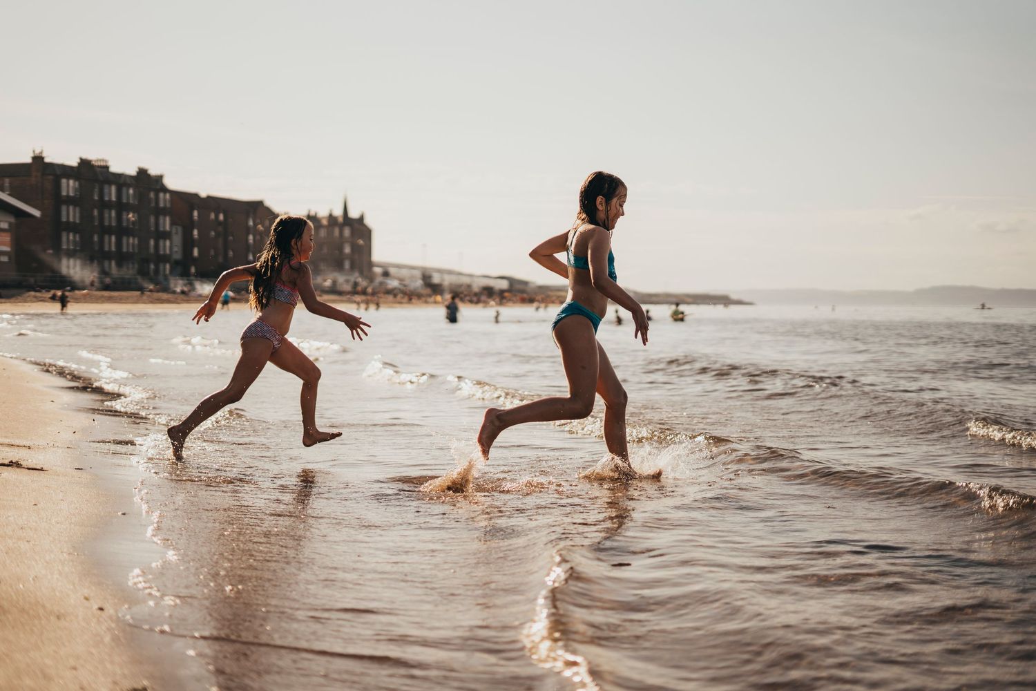 People running playfully through shallow ocean waves at sunset on a beach.