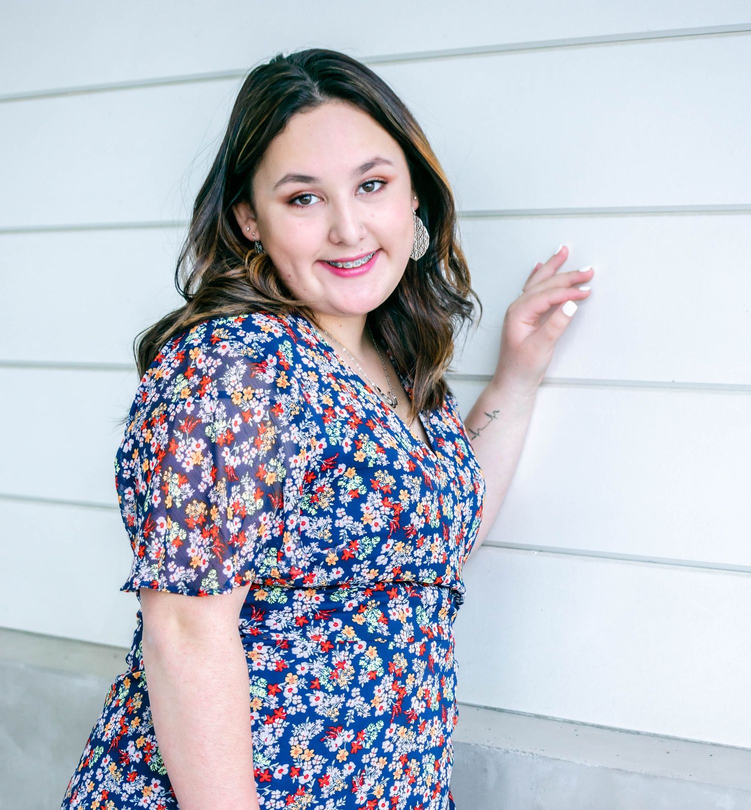 Floral print top styled casually with natural lighting against white wall backdrop.