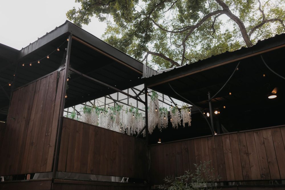 Rustic outdoor wedding venue with wooden walls, string lights, and lush tree canopy.