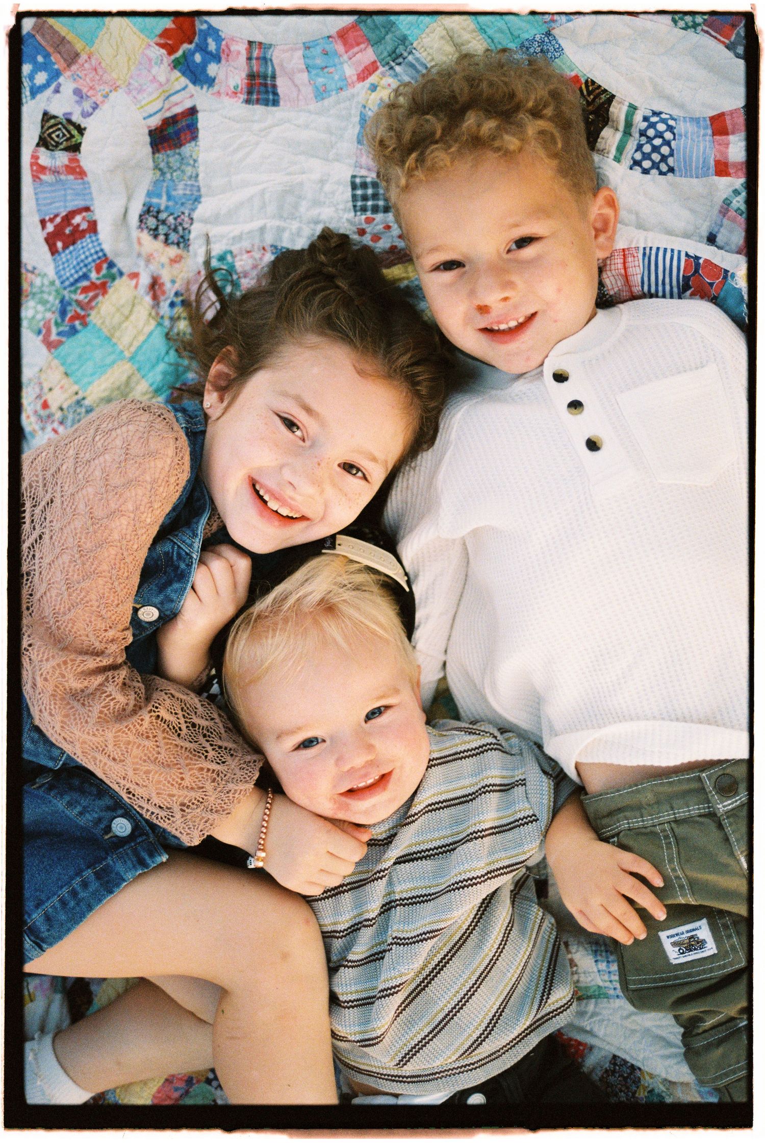 Children lying together on a colorful patchwork quilt, sharing sweet moments and laughter.