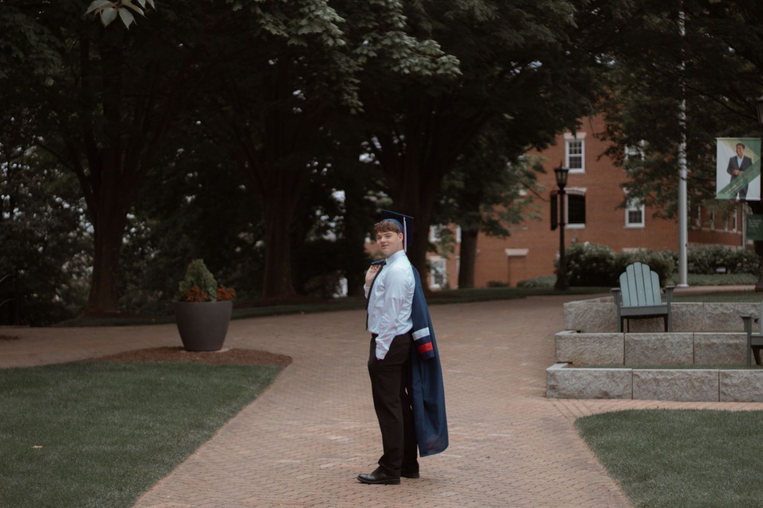 Graduate in academic regalia standing on a brick pathway near campus buildings.