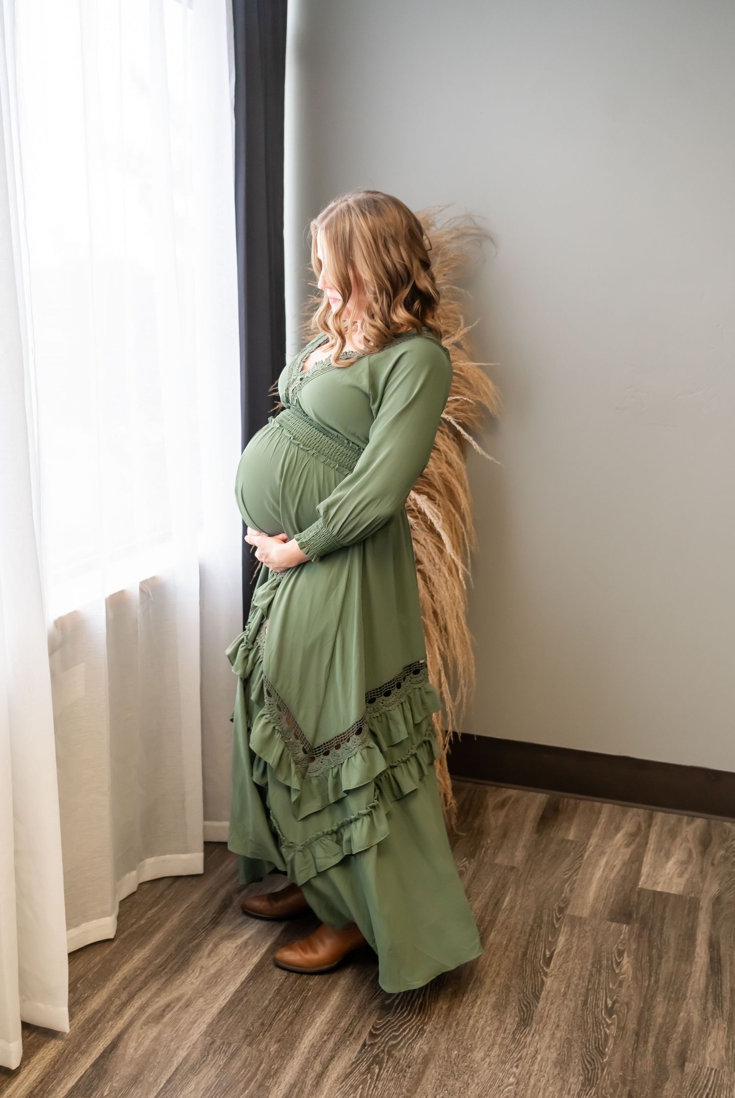 Indoor maternity photo with flowy sage green dress and natural light from window.