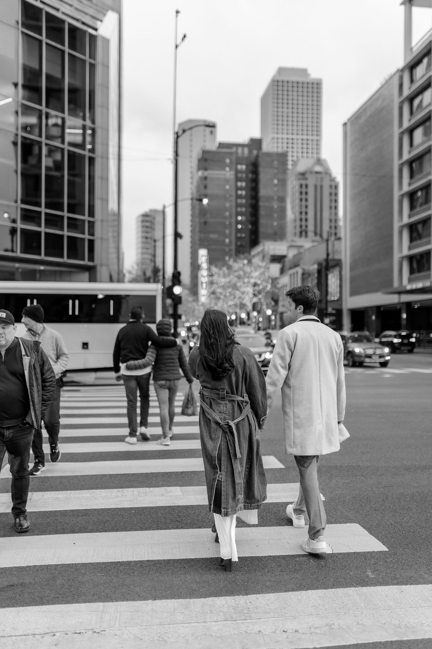 People walking across a crosswalk in a downtown cityscape with tall buildings in black and white.