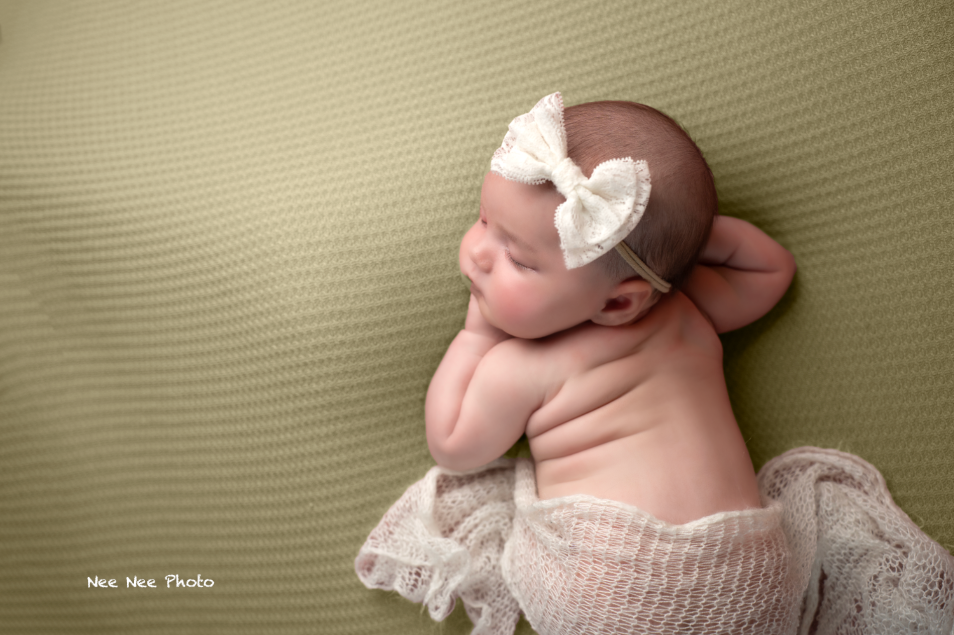 Sleeping newborn baby with white bow headband on green background, professional newborn photography. Embracing Life’s Beauty