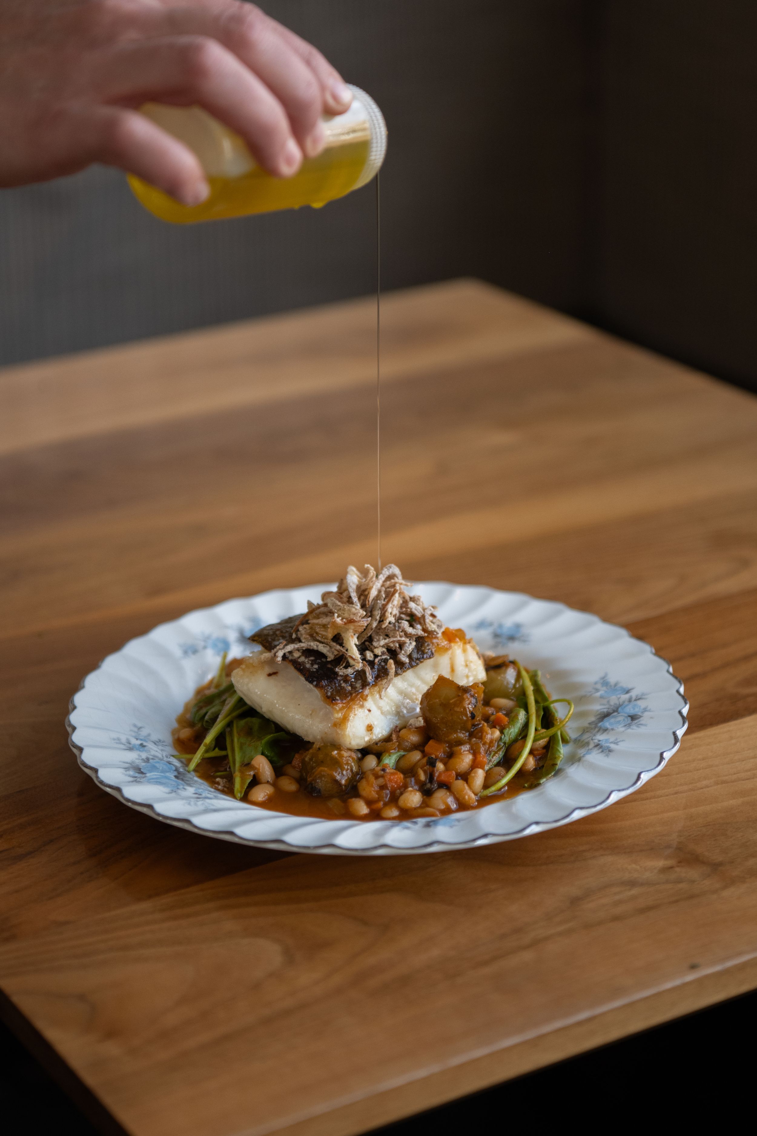 Drizzling olive oil over a plated dish of mushrooms and greens on a rustic wooden table.