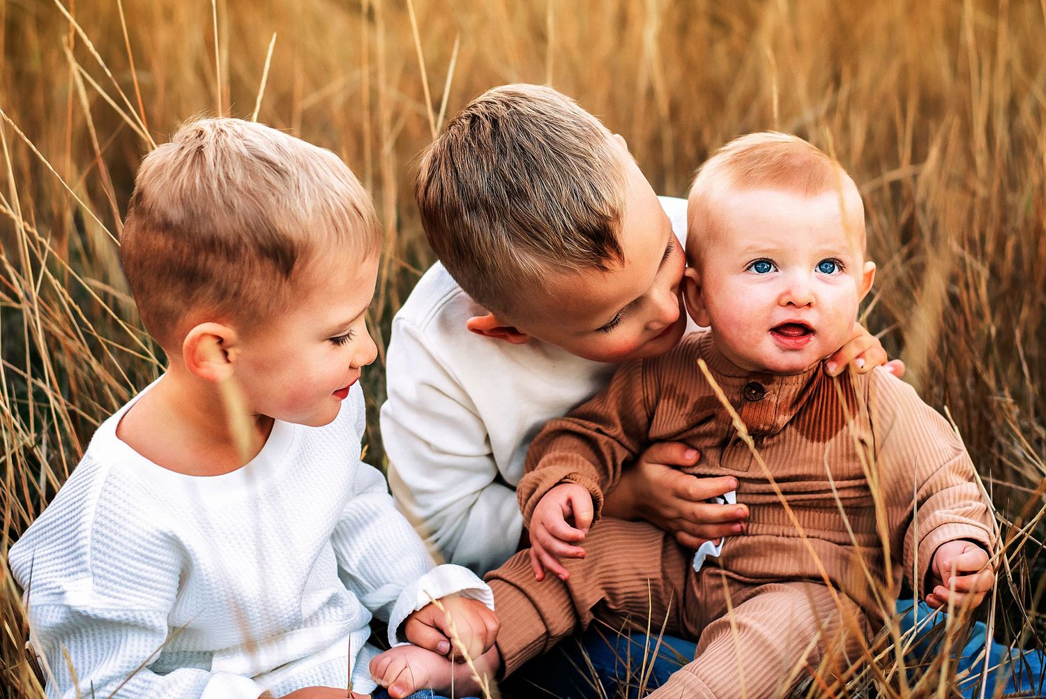 three young boys sitting in a grassy field on a warm sunny evening during a family photography session in Ellensburg, WA